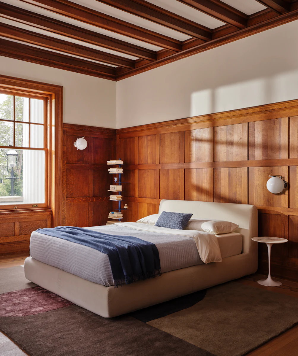 Headboard area of a bed with a beige upholstered bed and a black arching handle on the headboard front