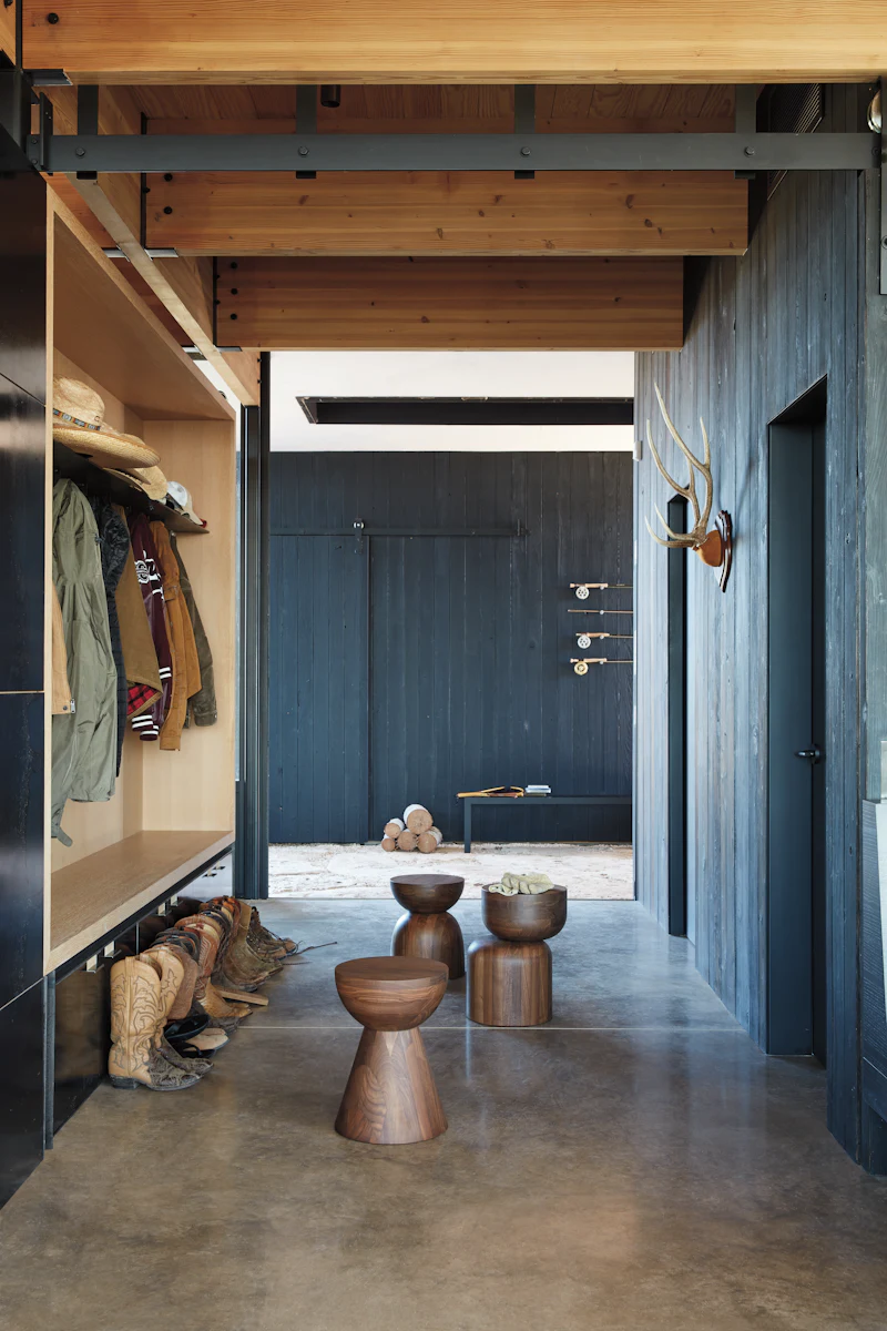 Cozy entry or mudroom with wooden stools and a dark round side table, lots of coats and boots