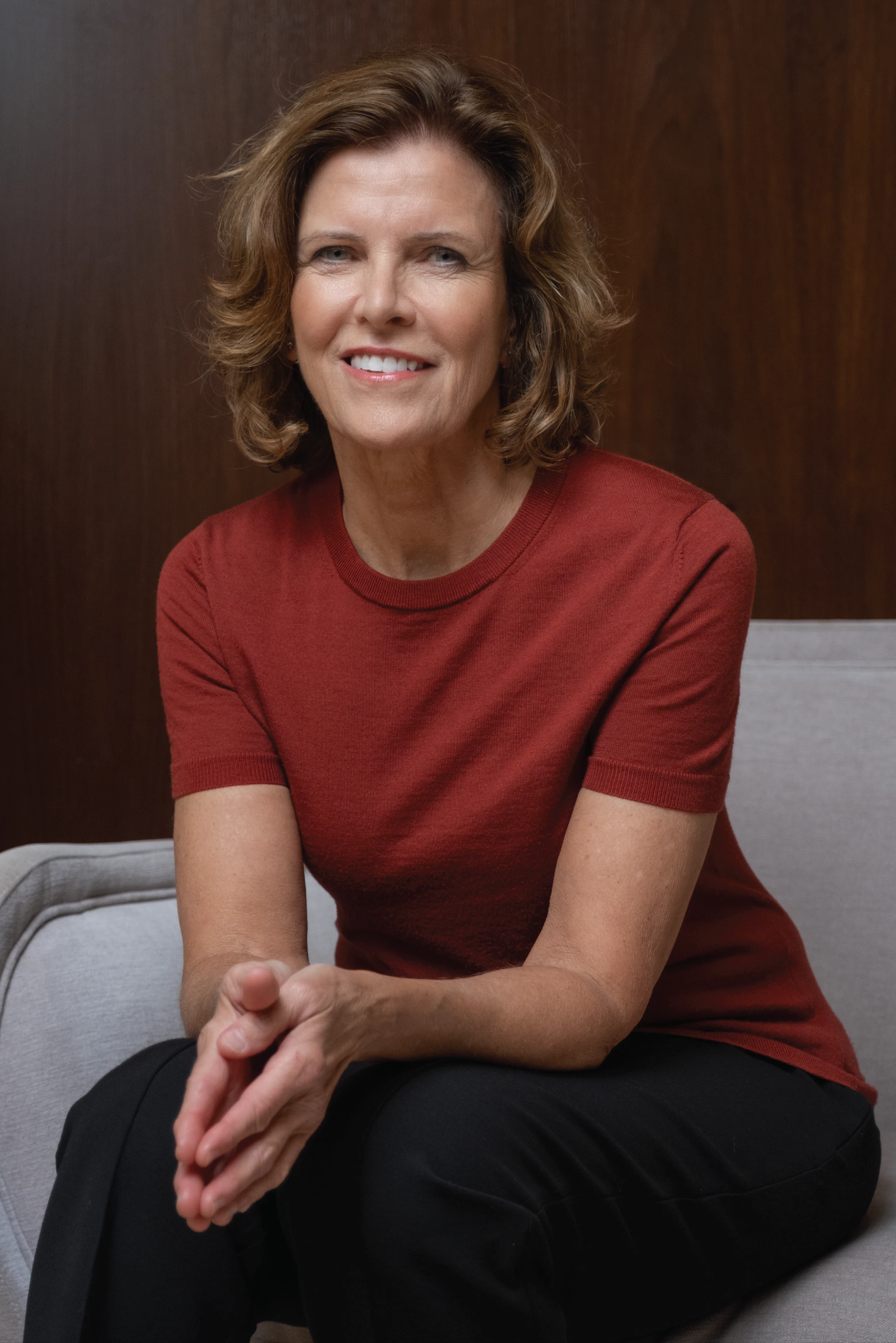Jeanne Gang, a member of the Board of Directors of MillerKnoll, Inc., wearing a red shirt and black pants while seated in a grey chair