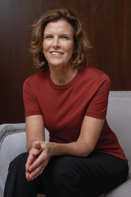 Jeanne Gang, a member of the Board of Directors of MillerKnoll, Inc., wearing a red shirt and black pants while seated in a grey chair