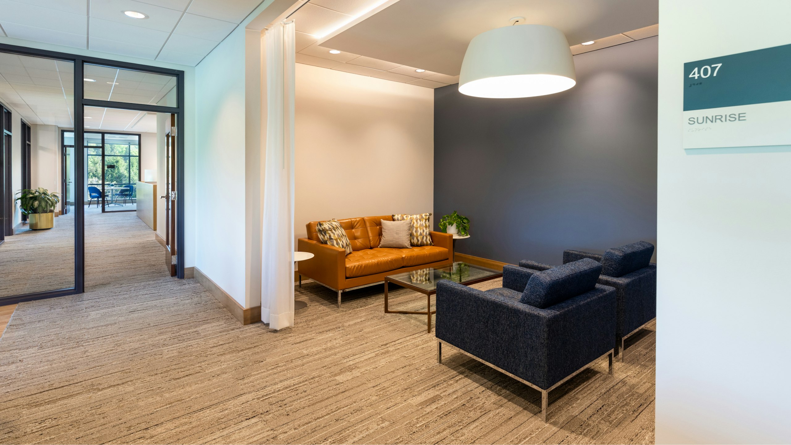 A communal seating area furnished with blue Florence Knoll lounge chairs and a glass coffee table