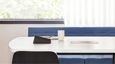 A coffee mug and assorted work papers atop a black and white Knoll Grasshopper table that features a blue Geiger Tuxedo Component Lounge and white Knoll Bertoia chair in a group conference room setting designed to facilitate employee connection.