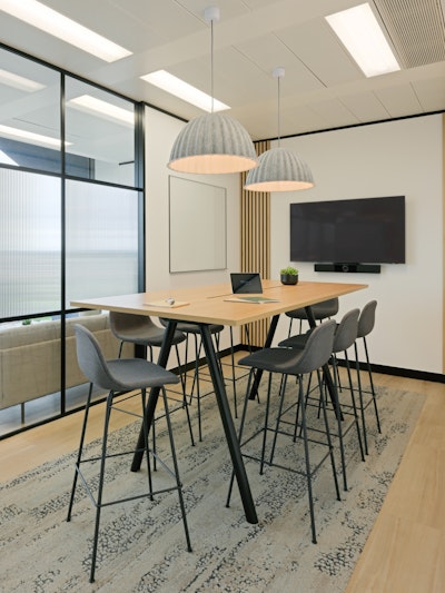 Eight counter height stools arranged around a large table, overheading lighting, and a mounted TV in a conference room in the NATO Defence Innovation Accelerator in London