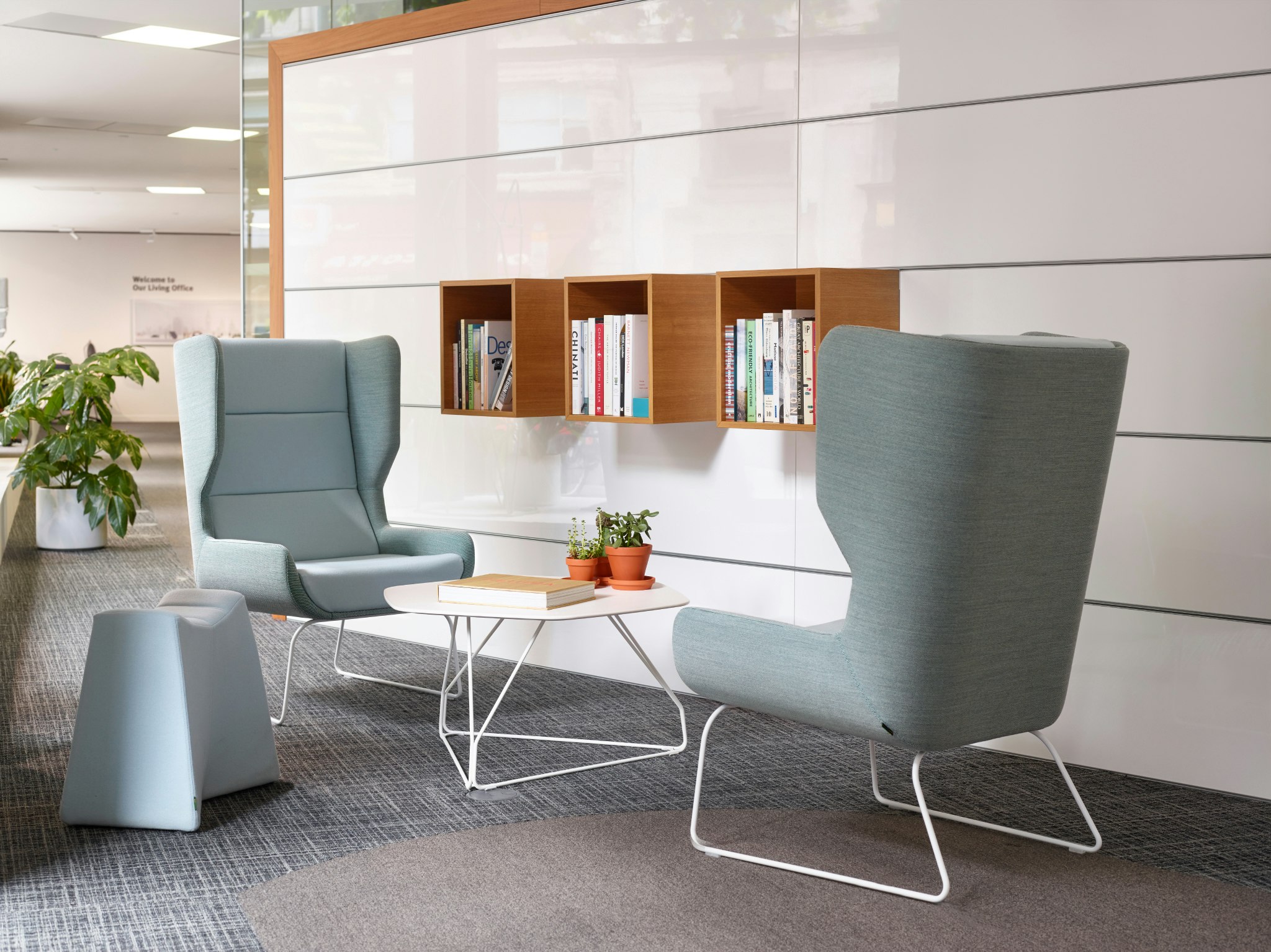 Two light blue Hush Chairs and a light blue Pinch Stool surround a Herman Miller white Polygon Wire Table in front of elevated book shelves.