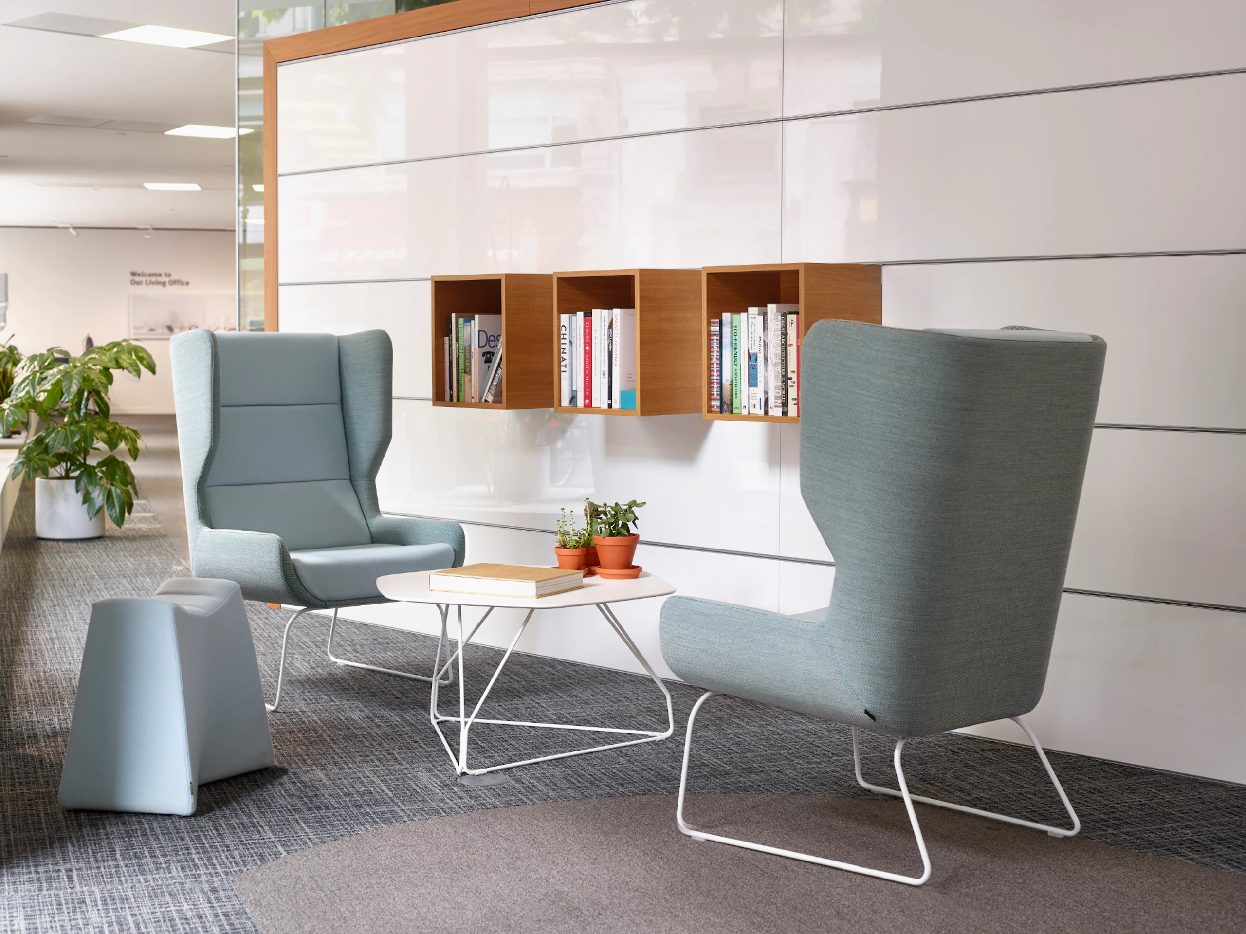 Two light blue Hush Chairs and a light blue Pinch Stool surround a Herman Miller white Polygon Wire Table in front of elevated book shelves.