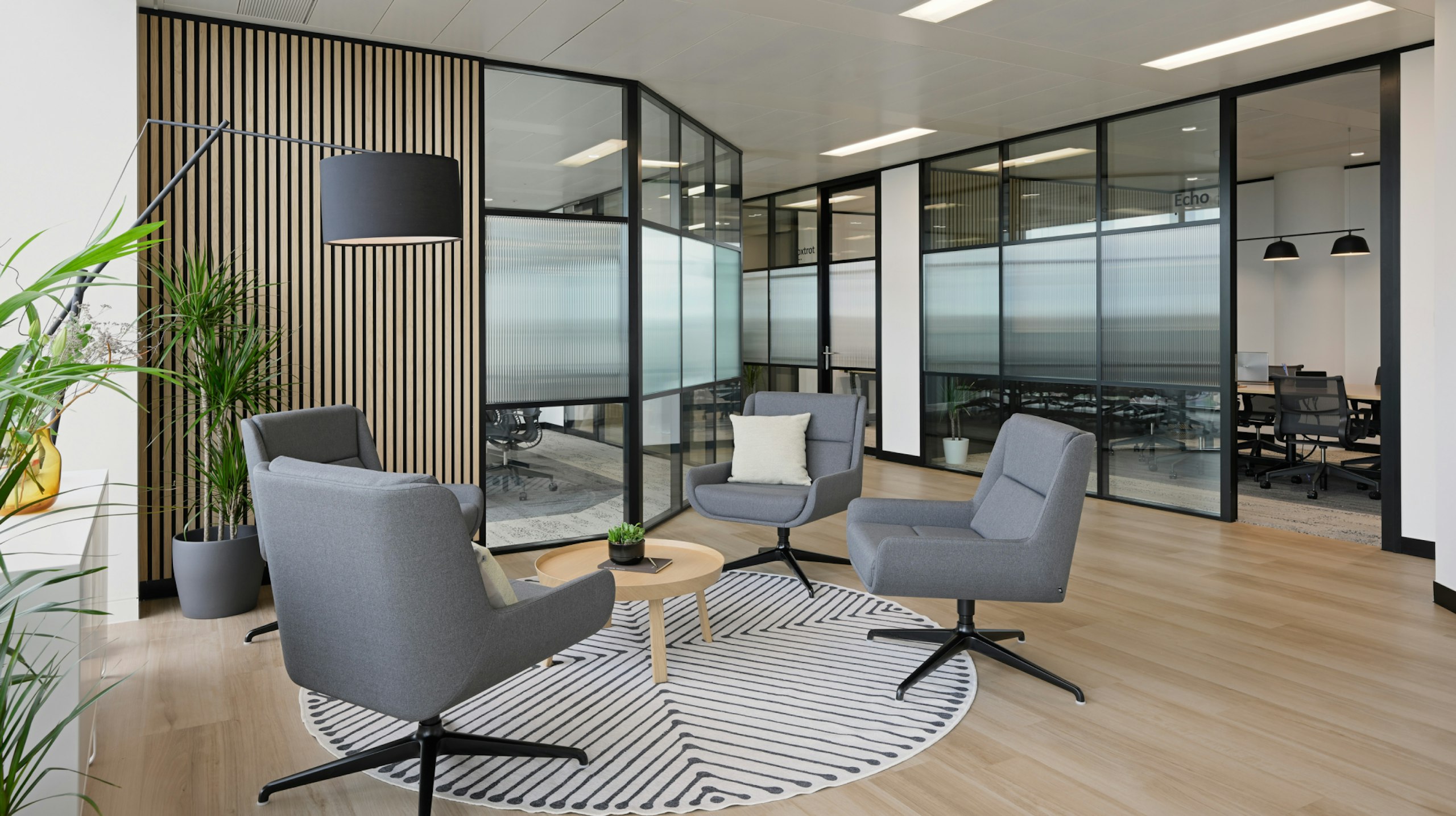 A seating area at the NATO Defence Innovation Accelerator in London furnished with four grey lounge chairs, a small side table, and green plants