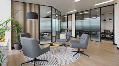 A seating area at the NATO Defence Innovation Accelerator in London furnished with four grey lounge chairs, a small side table, and green plants