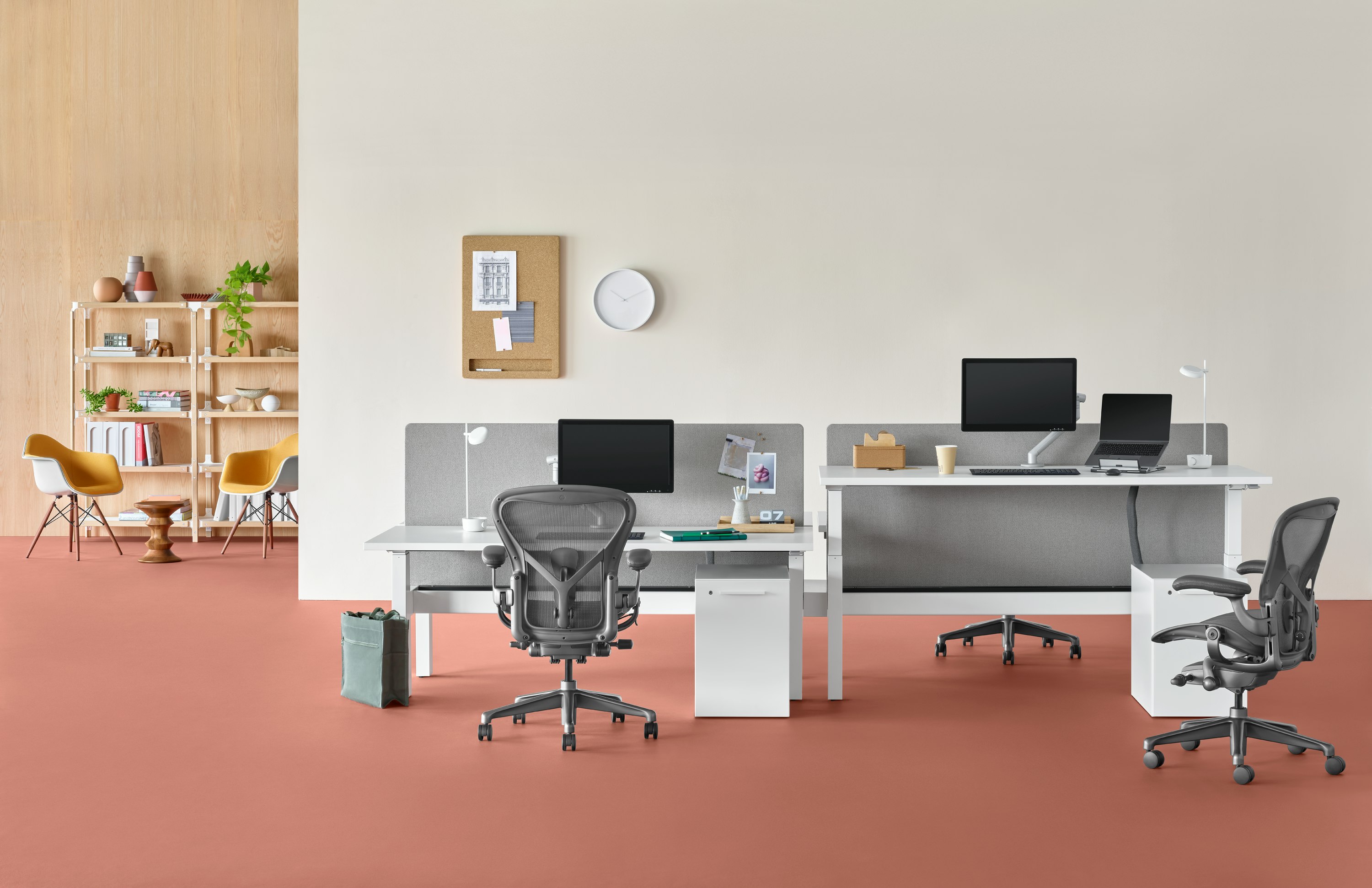 Standing desk system, Nevi Link, with rectangular work surfaces and four Aeron Chairs. One of the four desks is raised at a standing height.