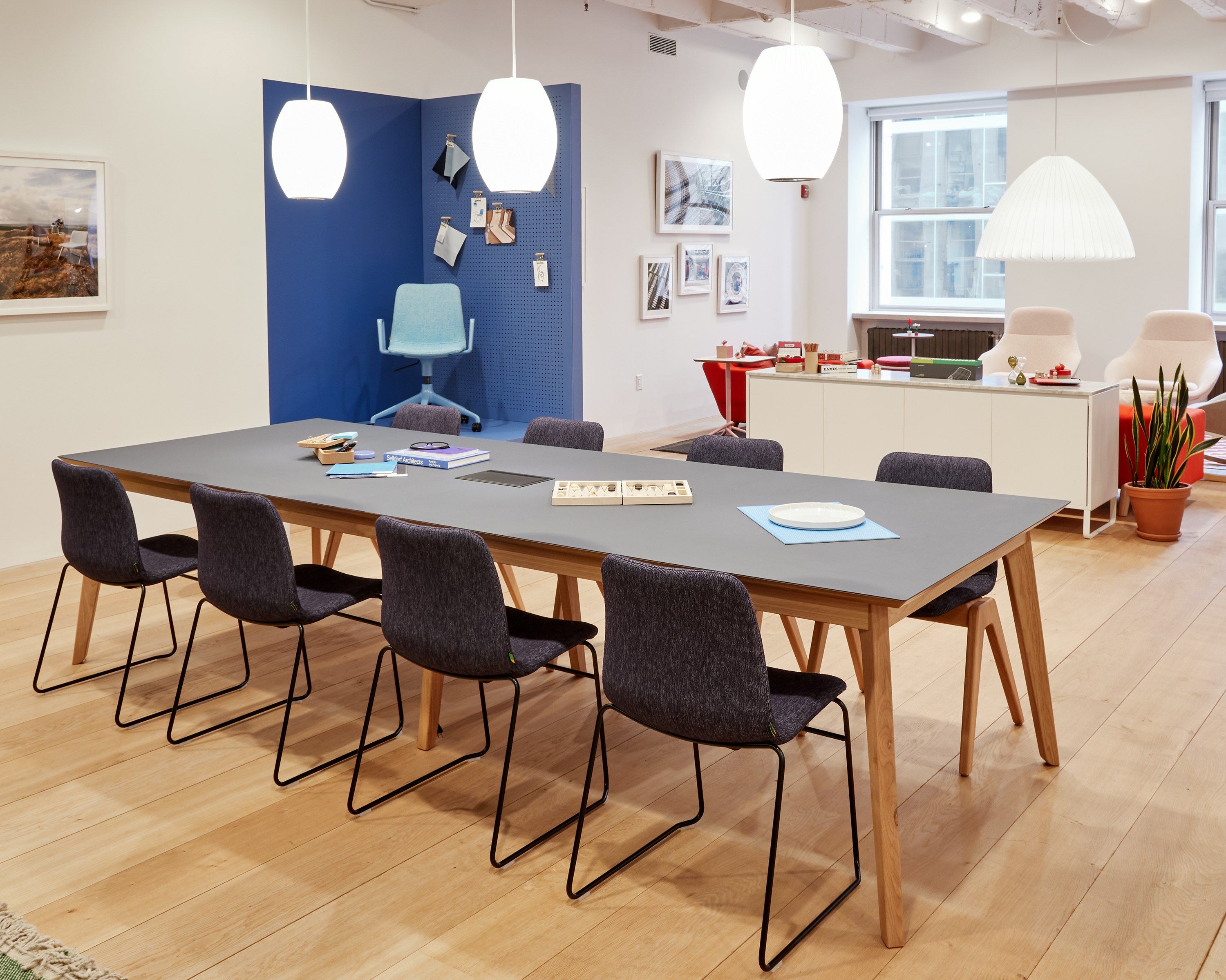 Eight upholstered Viv Chairs with black sled bases, around a large Dalby table.