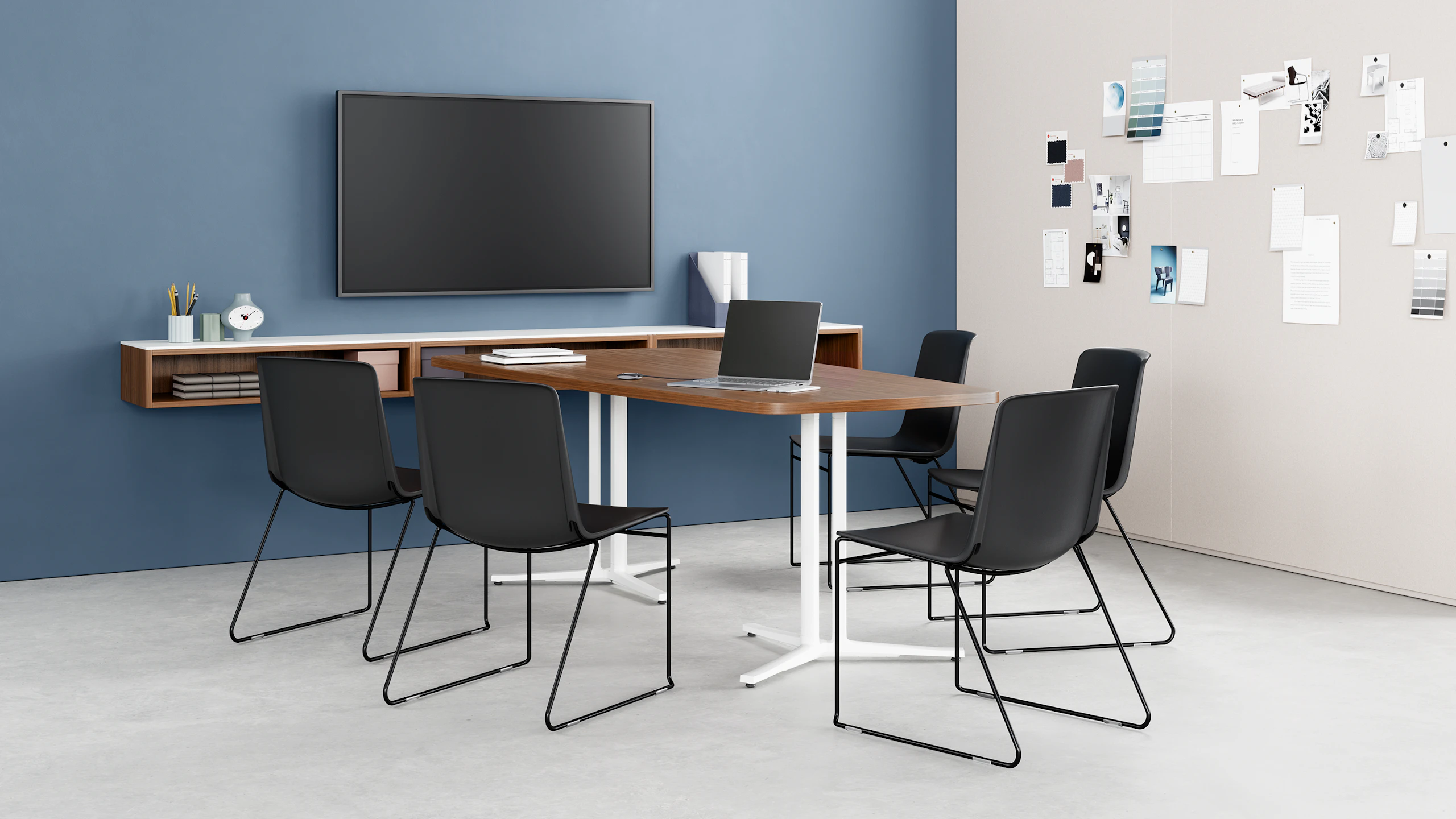 Black Pronta Stacking Chairs in a conference room with an Everywhere Table, tv monitor, and storage cabinet.