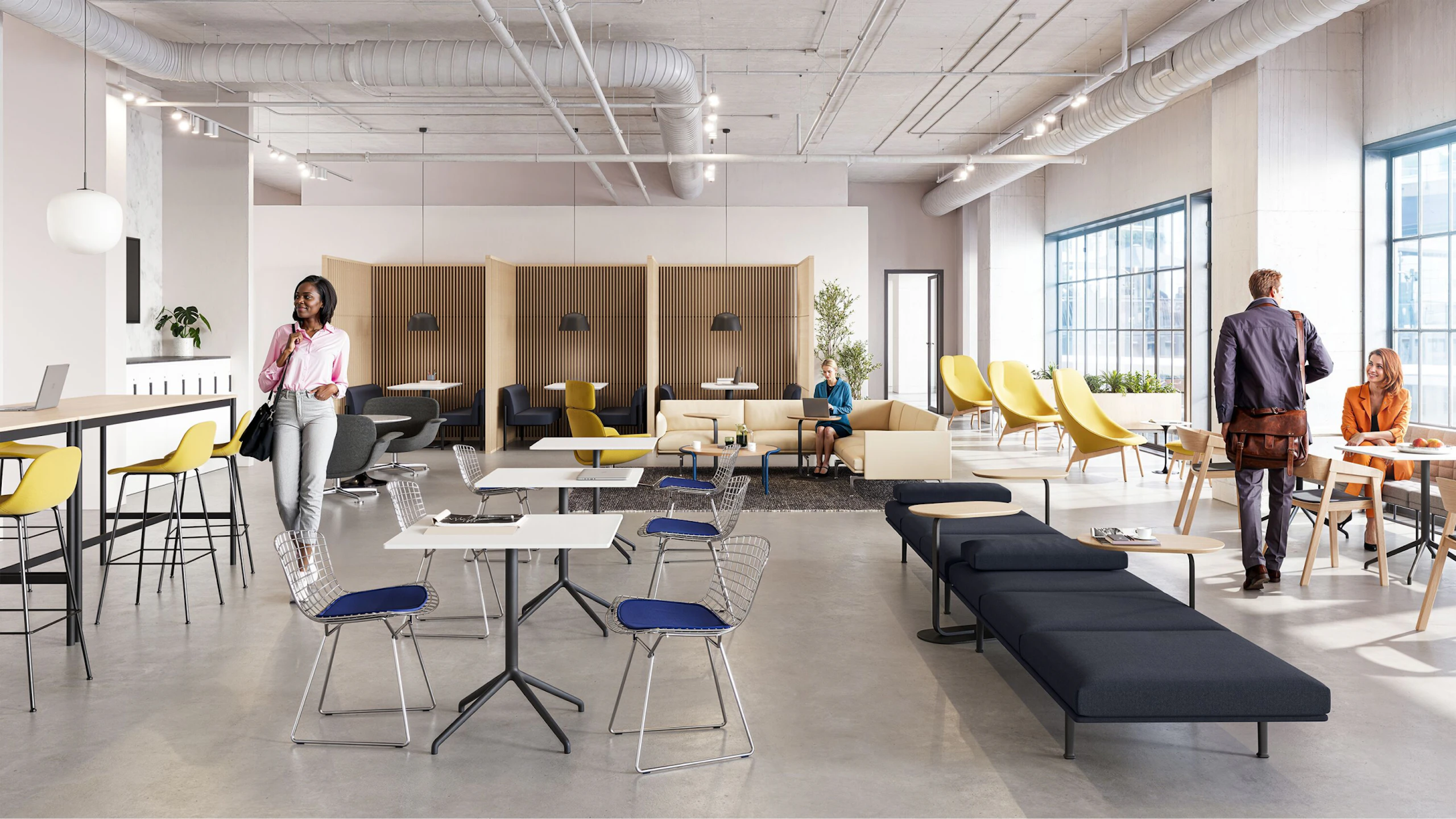 A brightly lit community setting featuring four people utilising a variety of colourful seating options including the HAY Uchiwa Lounge Chair, Muuto Base Tables and Muuto Still Cafe Tables