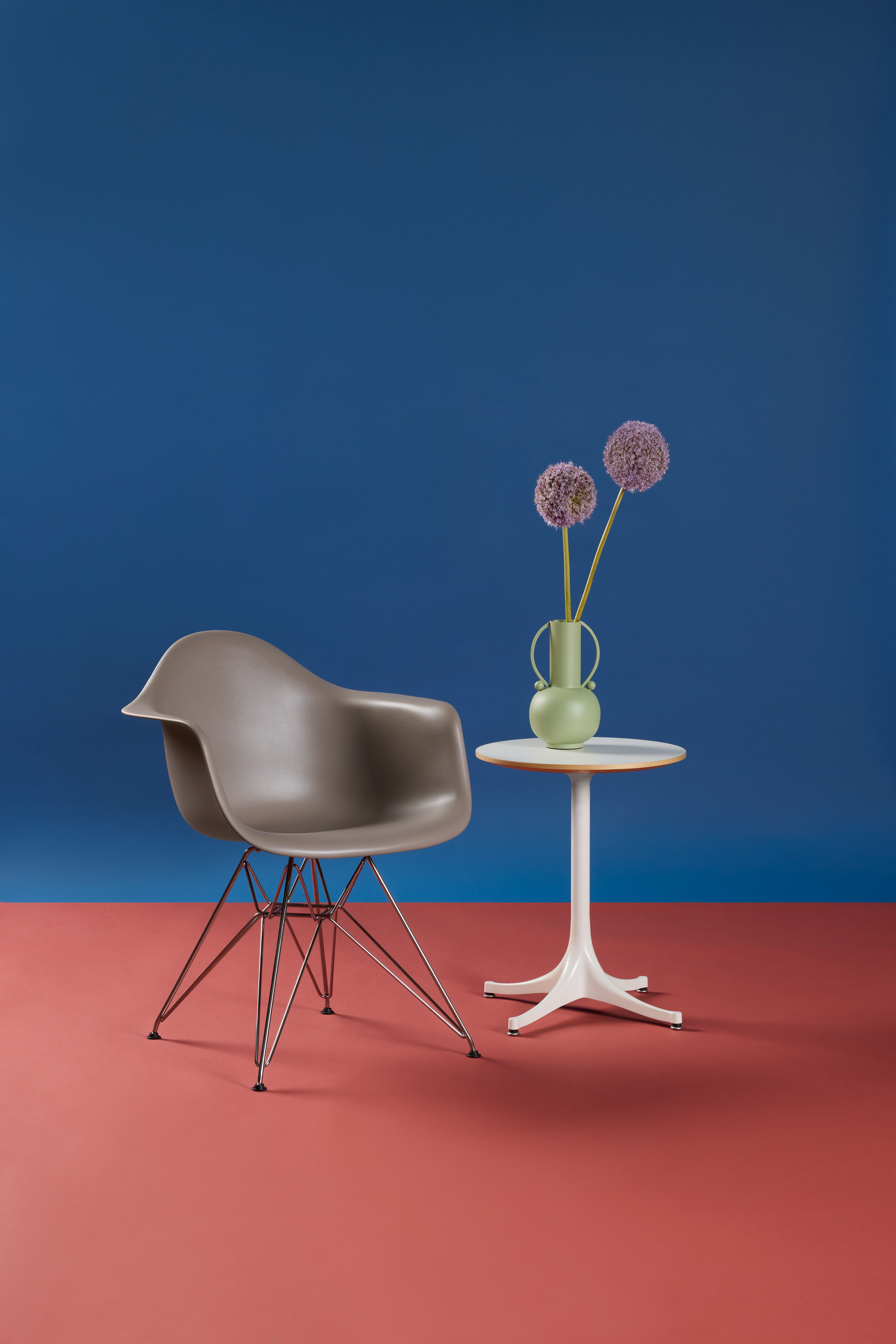 Single grey Eames Molded Plastic Armchair with blue background styled with Eames table.