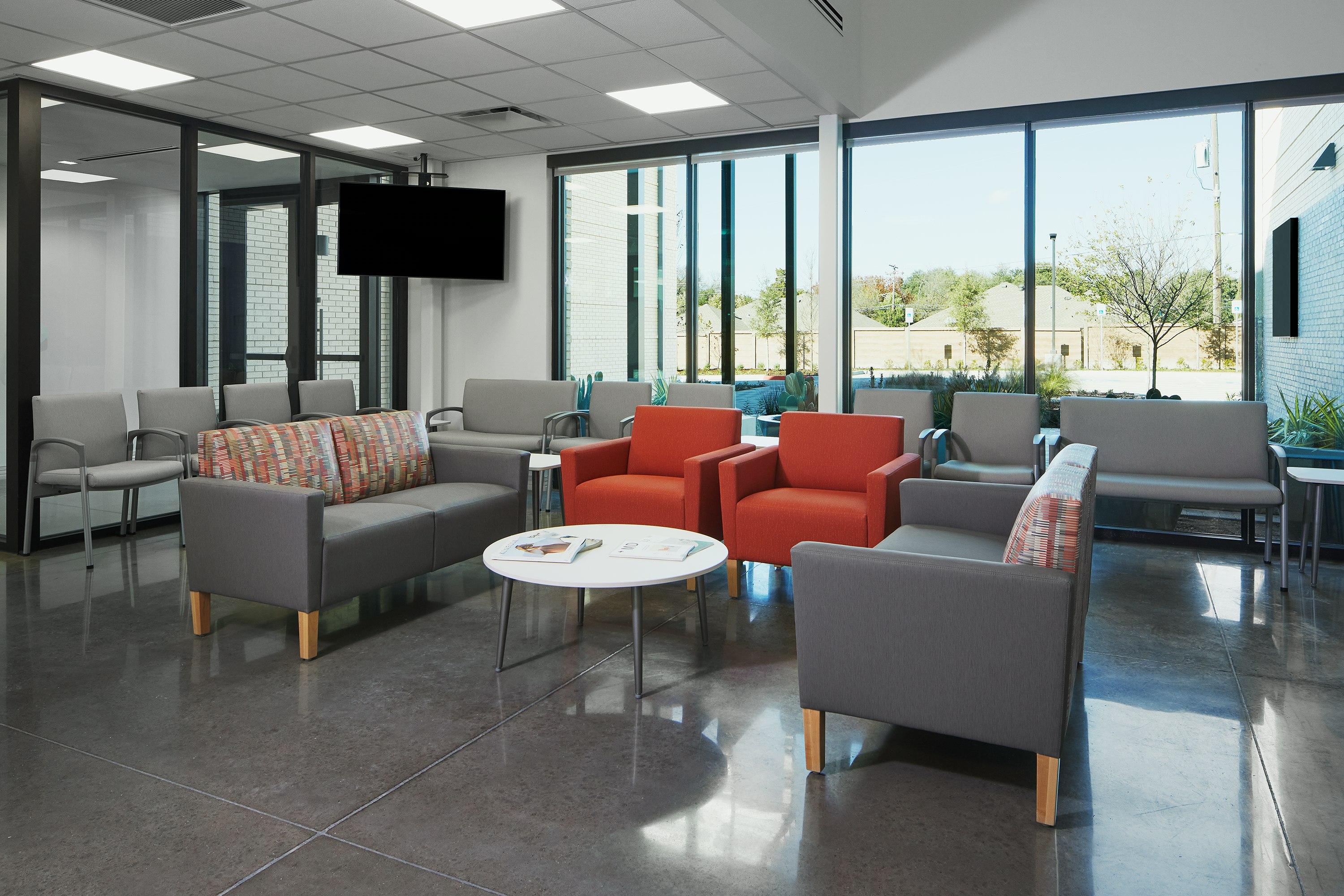 Lobby waiting area with Nemschoff Valor Side and Plus Chairs in gray, with Nemschoff Brava Classic Armchairs in orange and Nemschoff Brava Multiple Seating in gray seats and multicolored backs, with Nemschoff Palisade Coffee Table with a white top and silver legs.