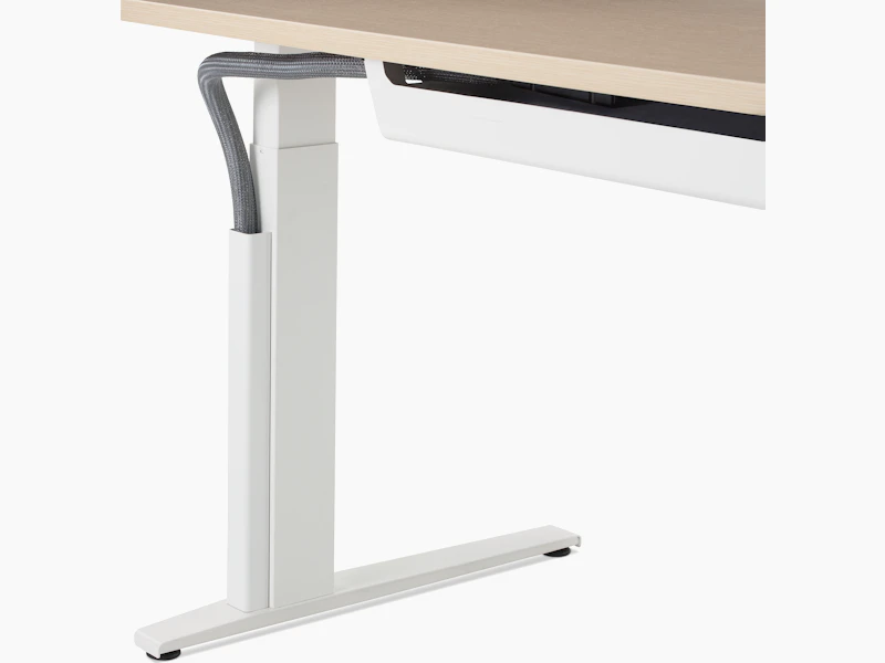 Close up of a mesh vertical wire manager attached to the white leg of a height adjustable table.