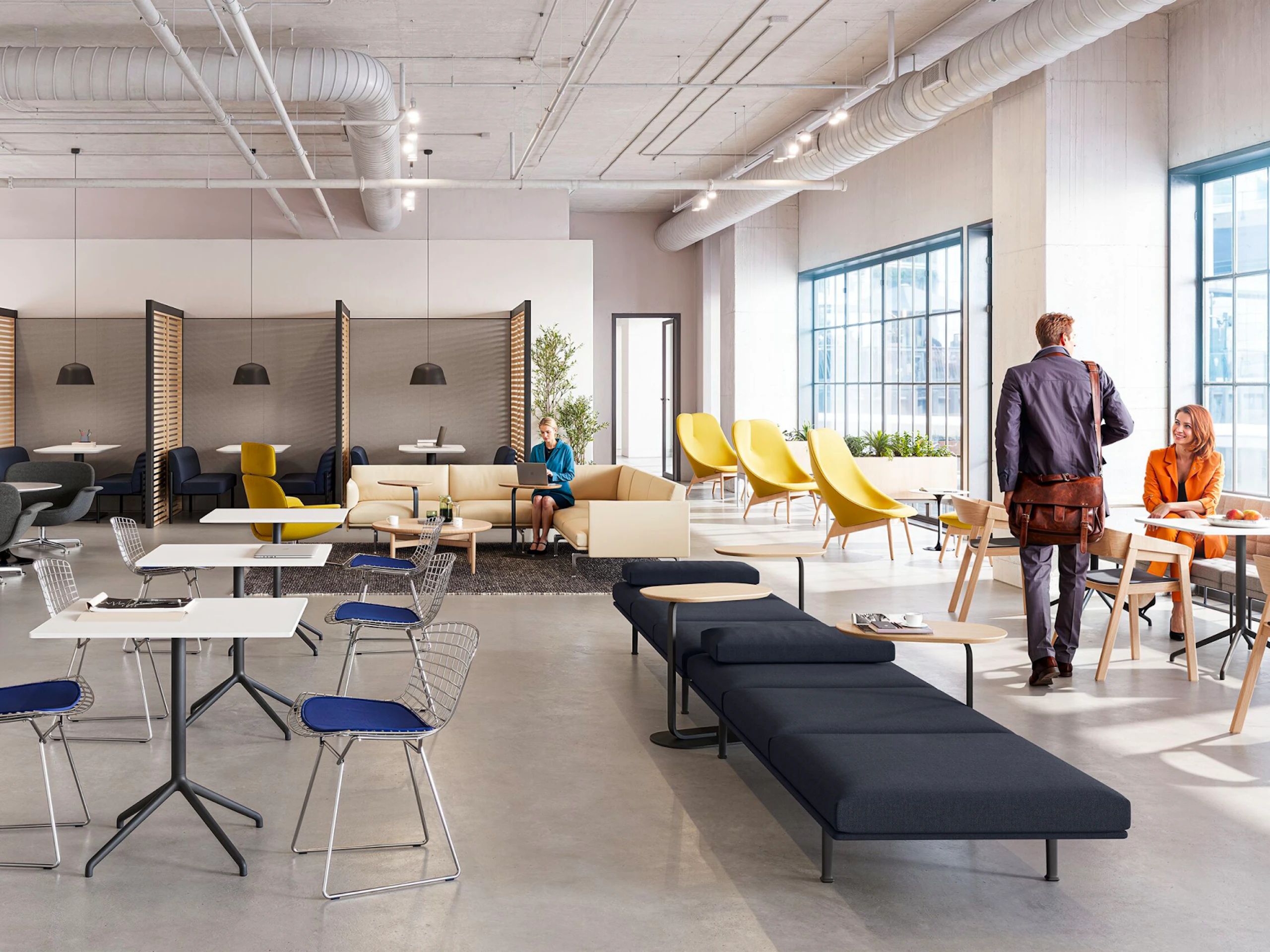 A brightly lit community setting featuring four persons utilizing a variety of colorful seating options including the HAY Uchiwa Lounge Chair, Muuto Base Tables, and Muuto Still Cafe Tables