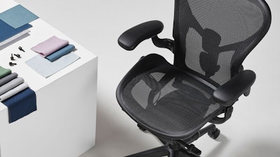 A black Aeron chair viewed from above, positioned next to a white display cube, on top of which an arrangement of folded Revenio textile swatches.