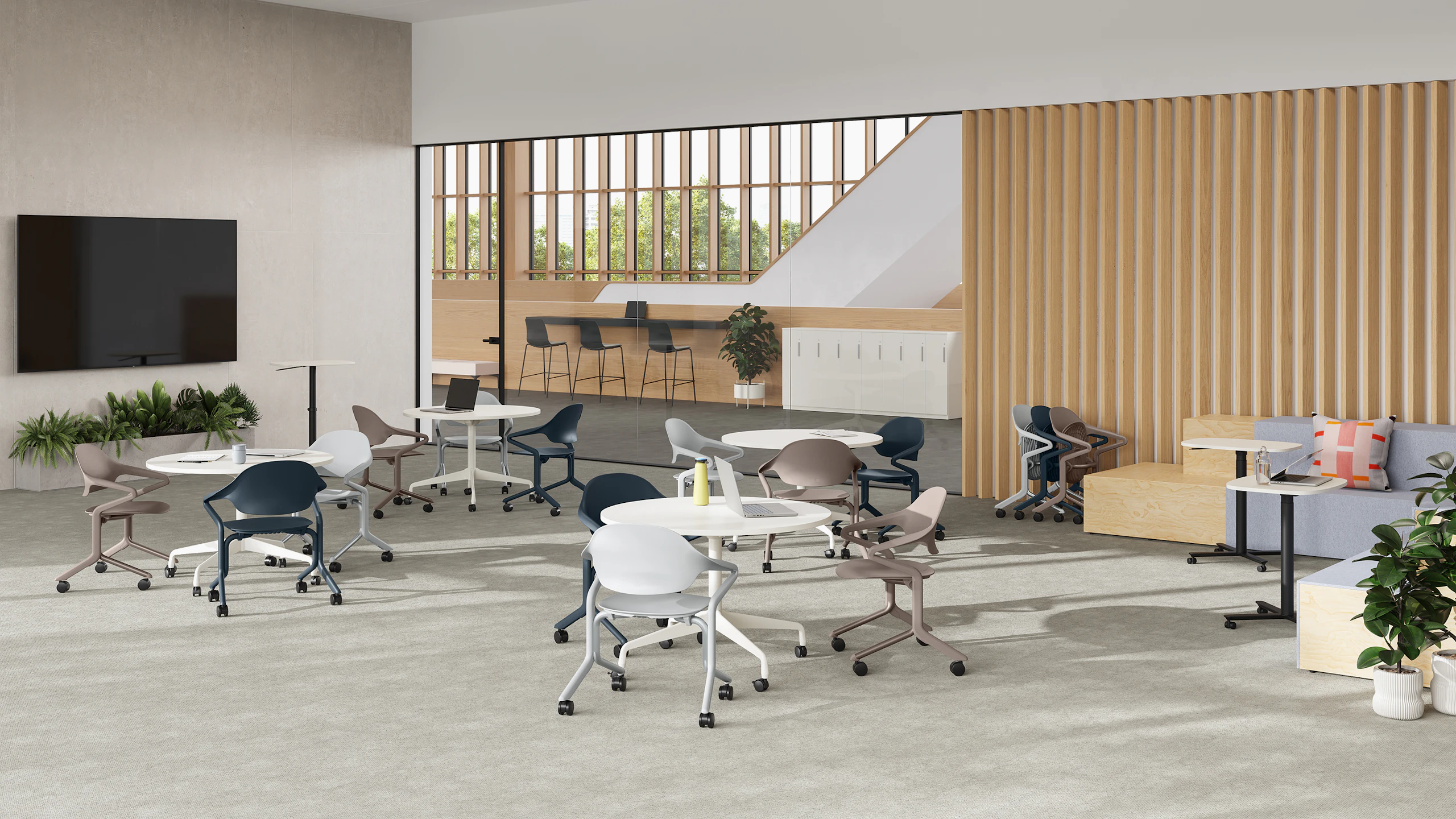 Fuld Chairs in alpine, nightfall and cocoa surround circular tables in a room with a large monitor , Passport table and Rockwell steps.