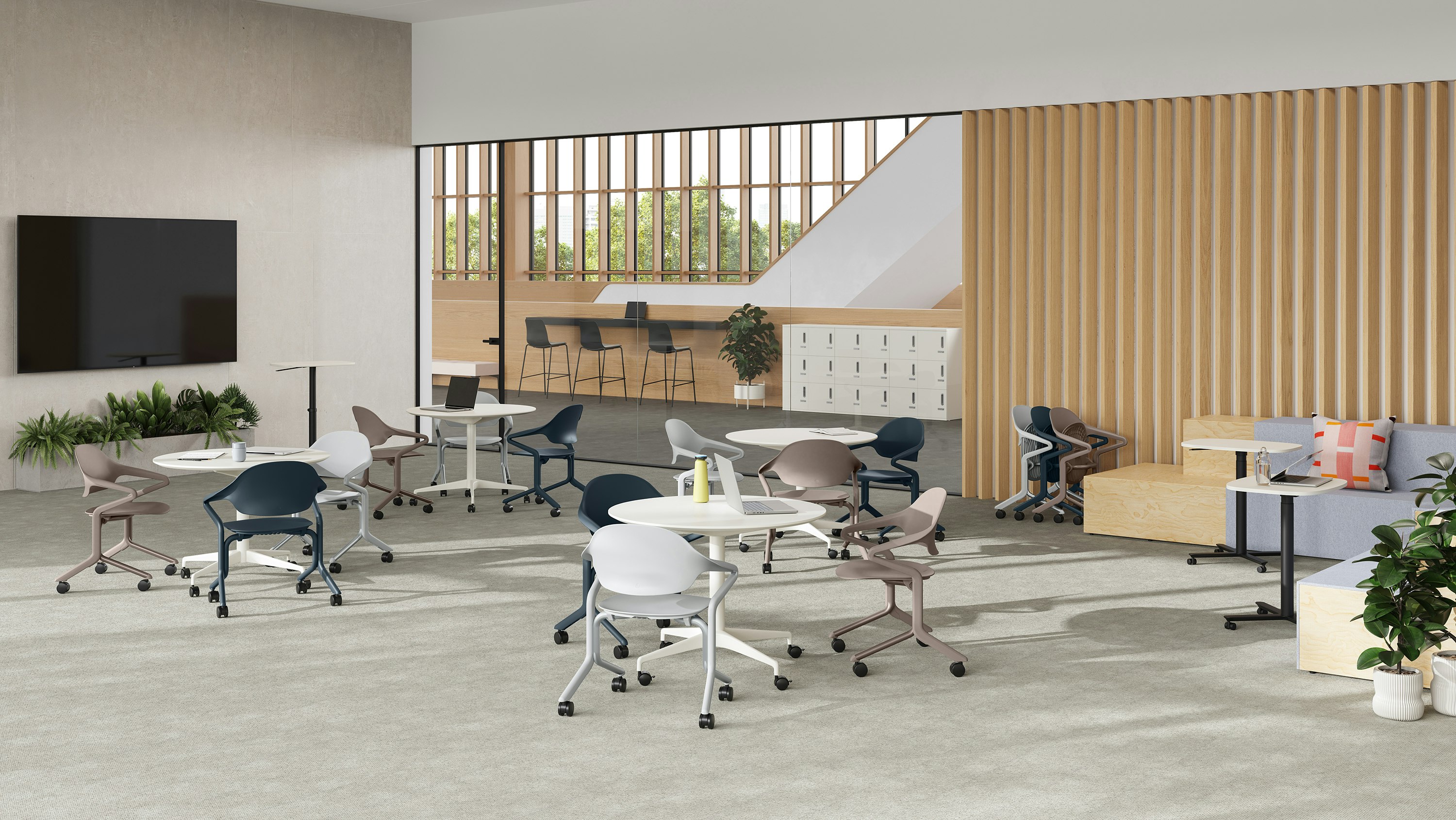 Fuld Chairs in alpine, nightfall and cocoa surround circular tables in a room with a large monitor , Passport table and Rockwell steps.