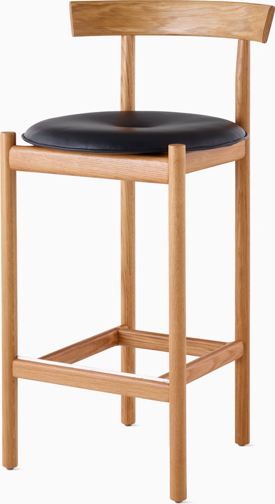 An oak Comma Stool with a seat pad, viewed from the front at an angle.