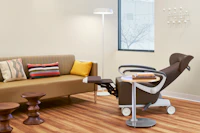 Patient room with a Nemschoff Ava Recliner in a brown upholstery with a Nemschoff Palisade Flop Sofa with a Steps Lounge System Table with an Ode Floor Lamp with two Eames Walnut Stools.