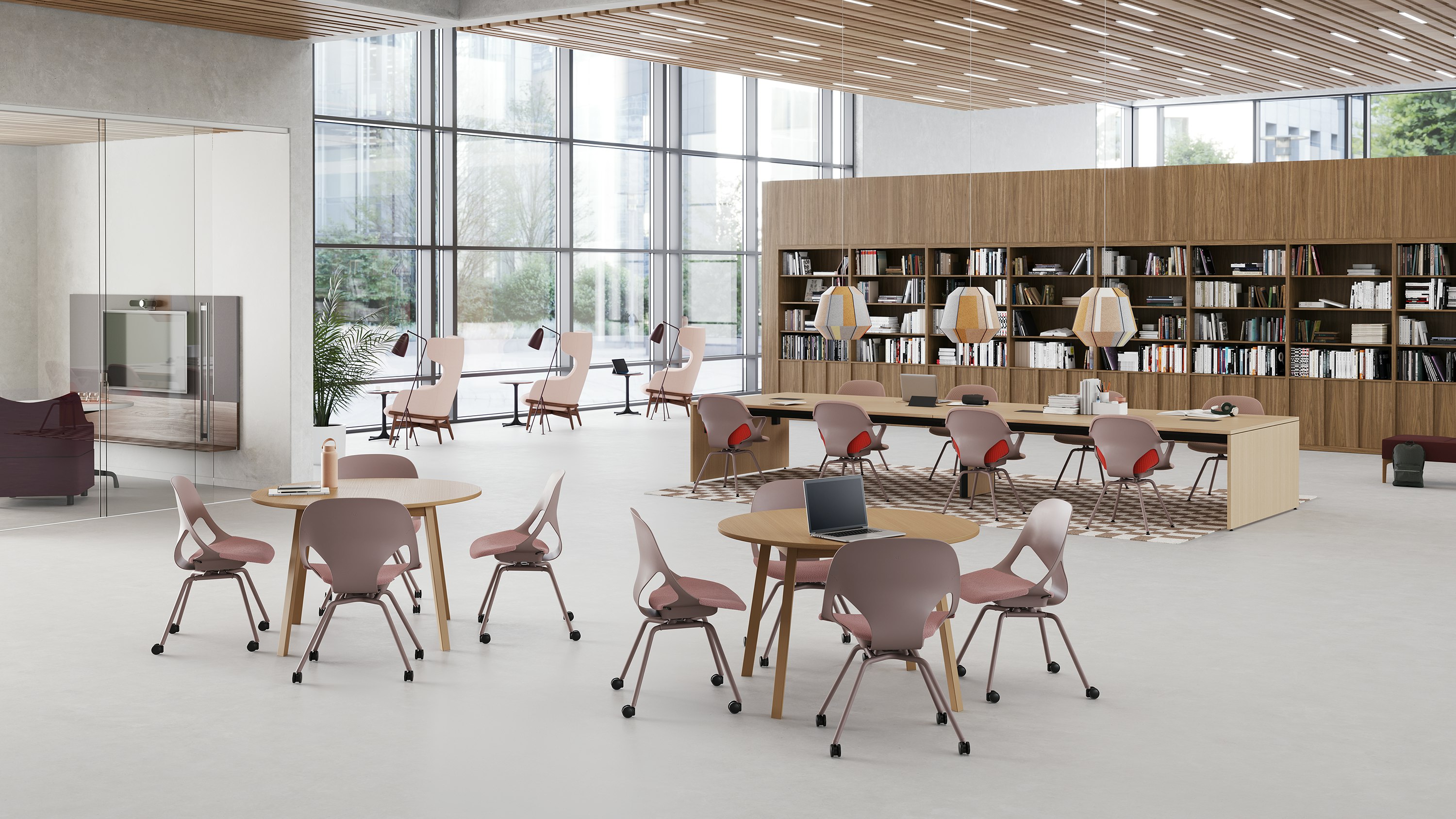 Two round table each with four light brown Zeph side chairs are in front of a long rectangular project table with eight light brown Zeph side chairs with light brown knit covers in a common area