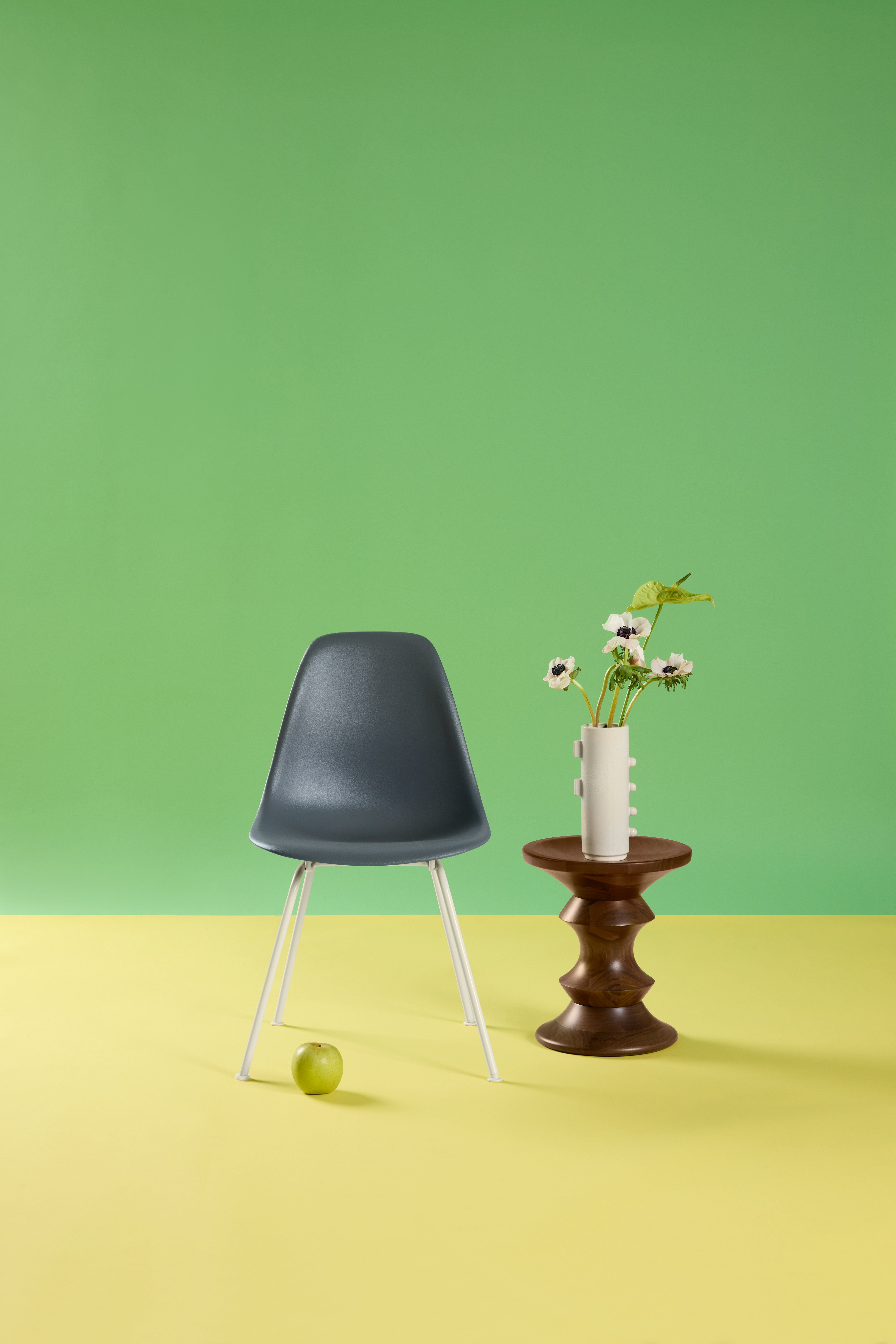 Single blue Eames Molded Plastic Side Chair with green background styled with Eames Walnut Stool
