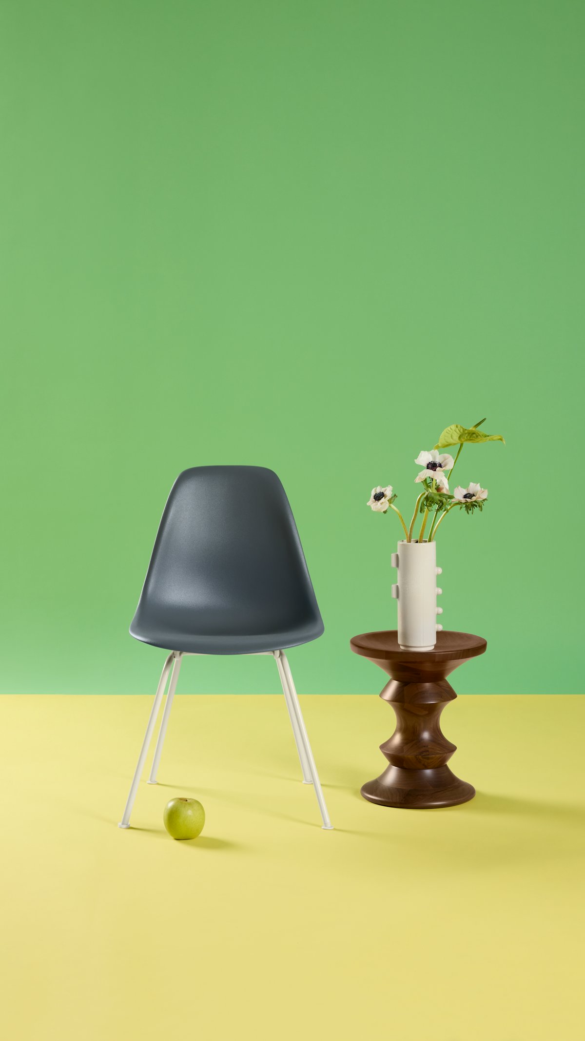 Single blue Eames Molded Plastic Side Chair with green background styled with Eames Walnut Stool