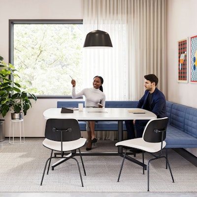 A group setting featuring two people sitting on a blue corner bench while participating in a virtual meeting in a conference room furnished with Geiger Tuxedo Component Lounge seating, a Knoll Grasshopper Table, and a Knoll Florence Knoll Credenza