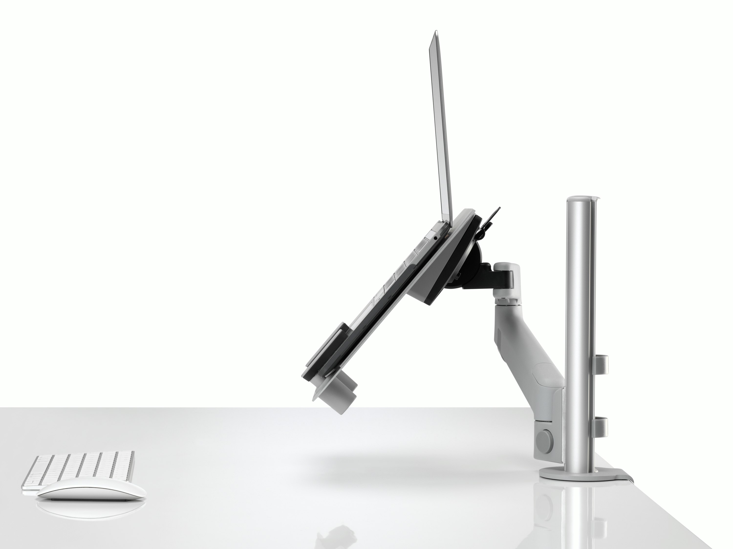 Profile view of an open laptop raised and supported by a grey Lima Laptop Mount connected to a Lima Monitor Arm.