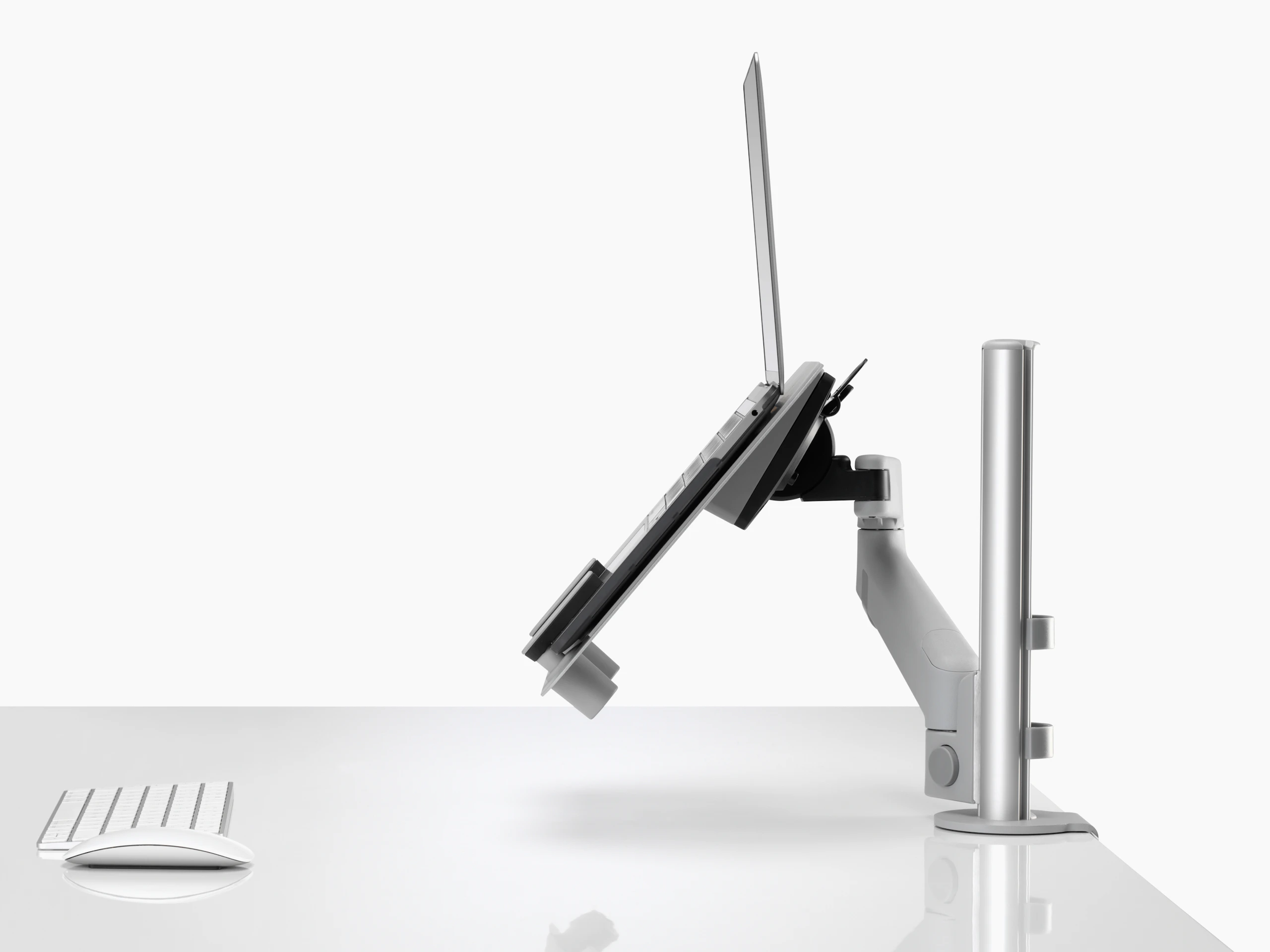 Profile view of an open laptop raised and supported by a grey Lima Laptop Mount connected to a Lima Monitor Arm.
