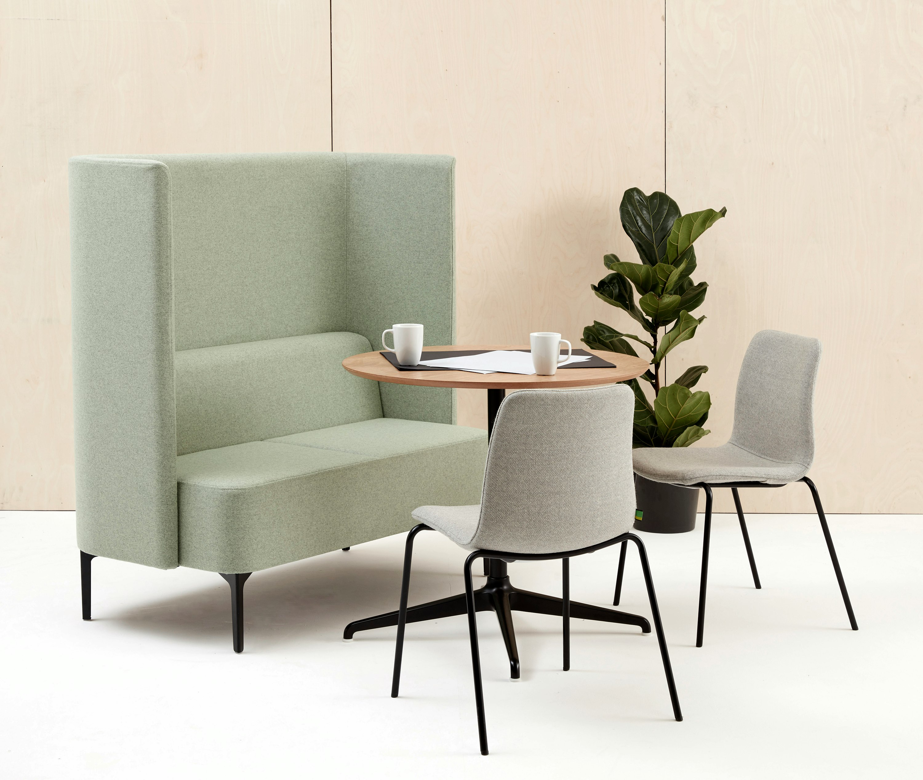 Two seat highback Pullman Sofa upholstered in pale green fabric, with black legs, sat with two Viv Side Chairs and a Ali meeting table.