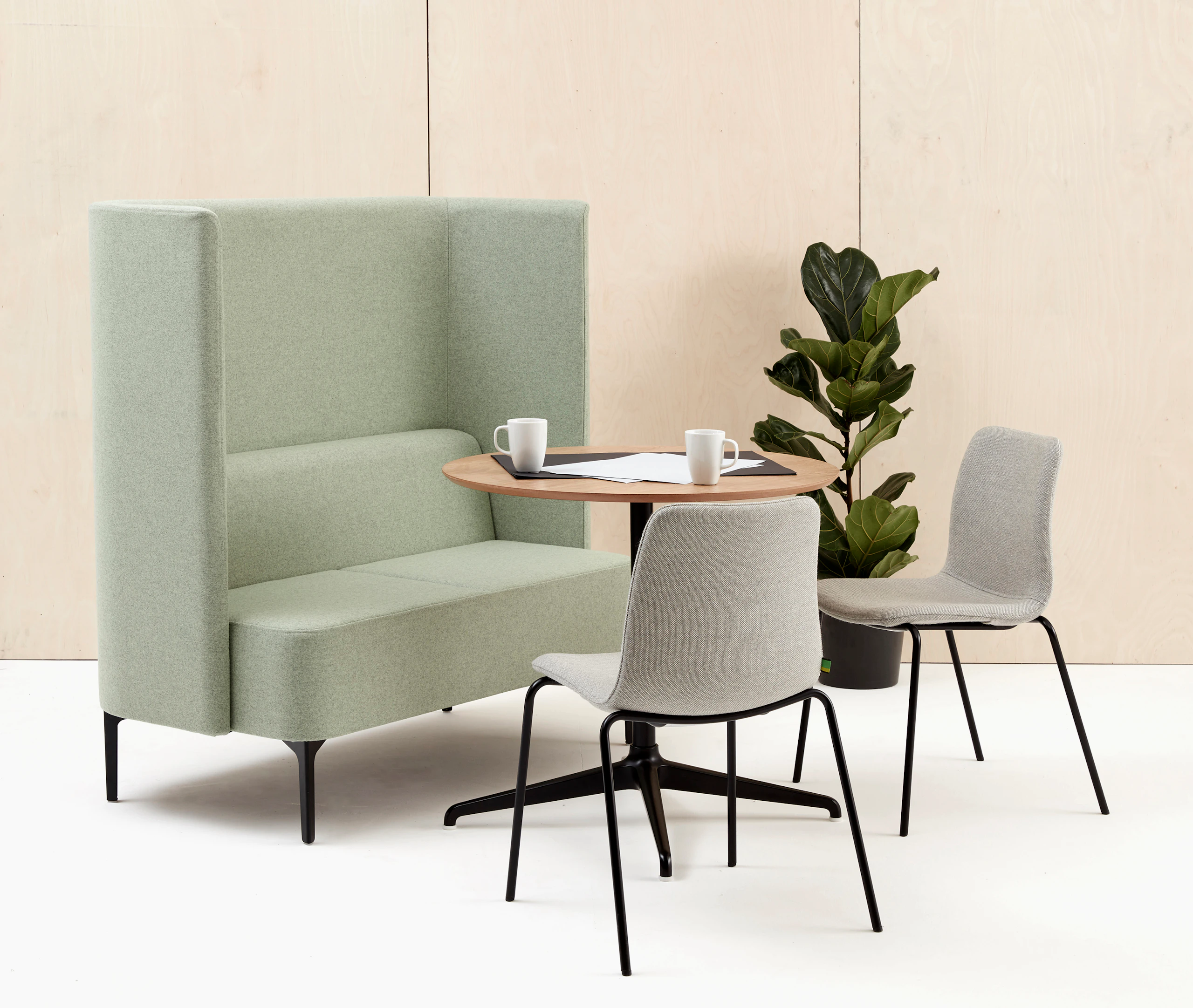 Two seat highback Pullman Sofa upholstered in pale green fabric, with black legs, sat with two Viv Side Chairs and a Ali meeting table.