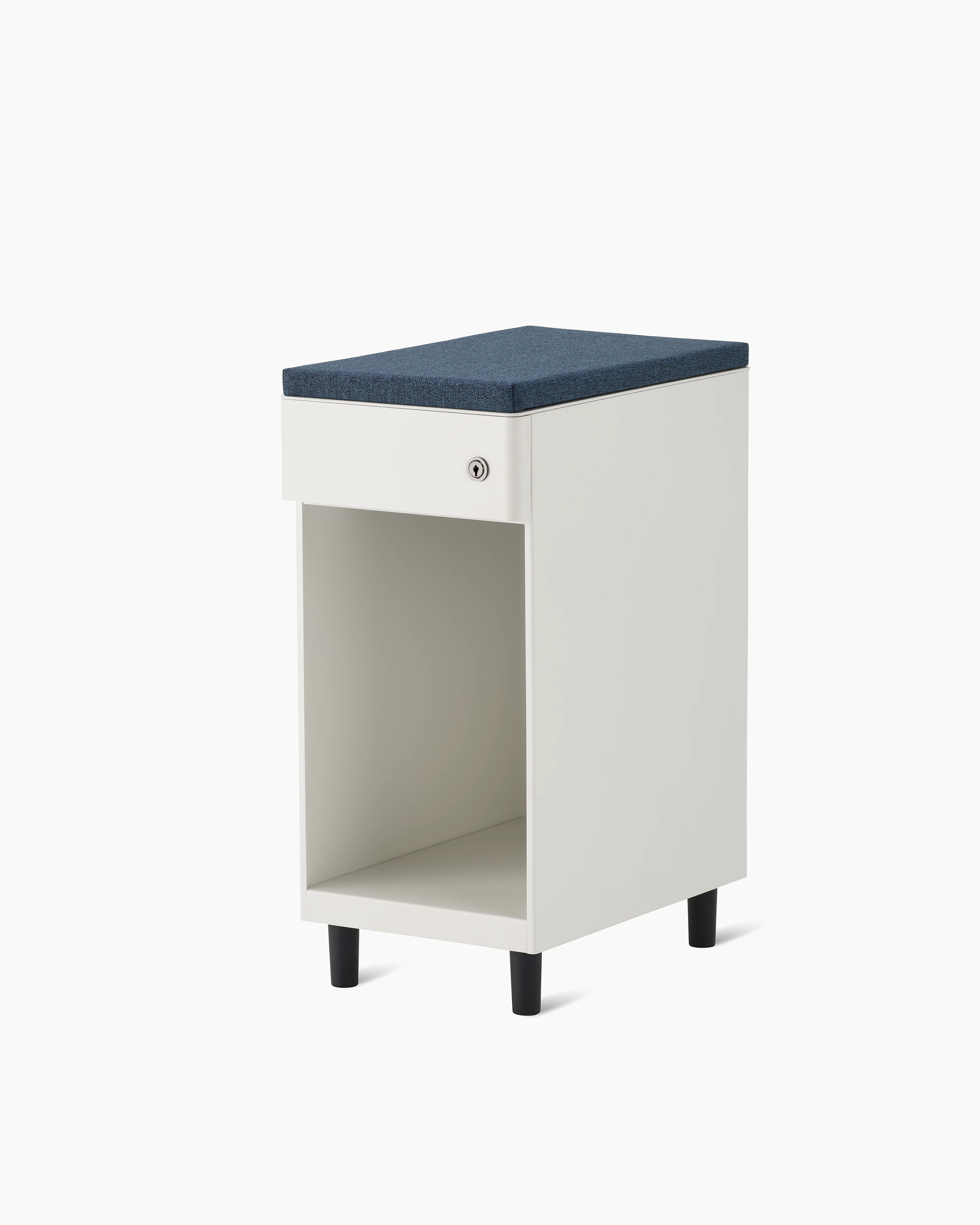 Slim, white storage pedestal on black feet with a drawer and a lock, a blue cushion top, and opening below drawer for storage.