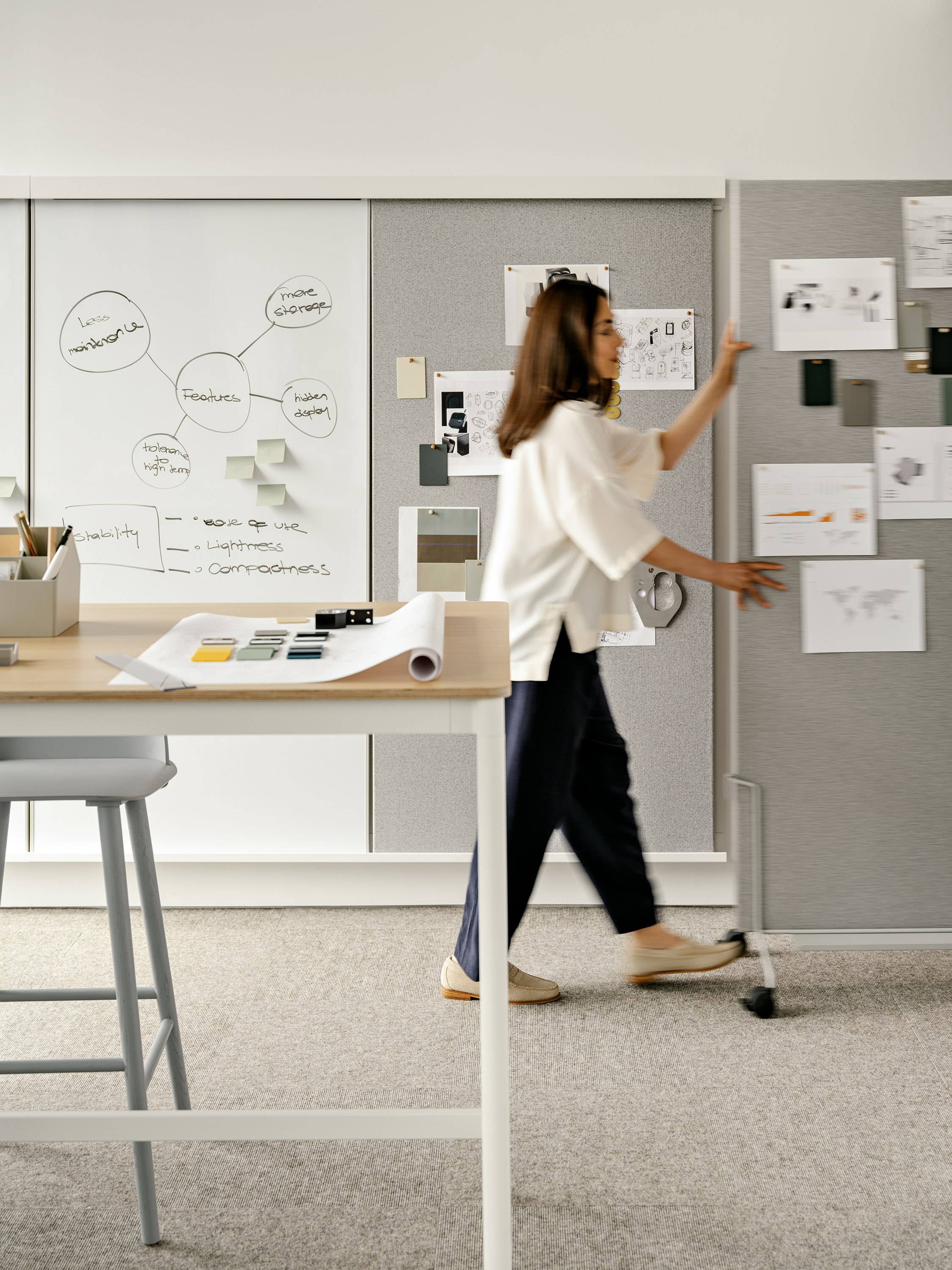 A woman pushing a grey OE1 wall on casters through an office setting.