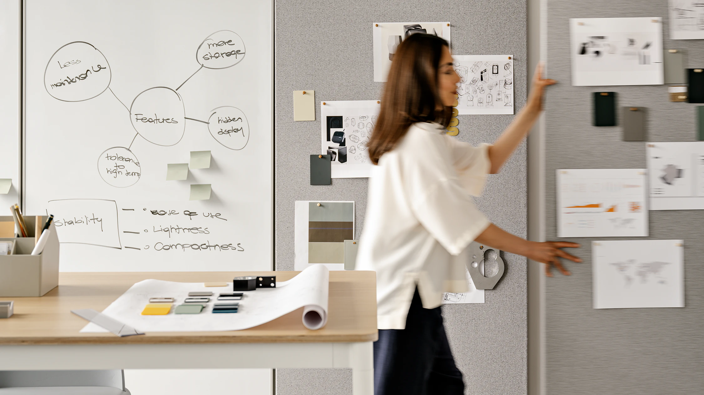 A woman pushing a grey OE1 wall on casters through an office setting.