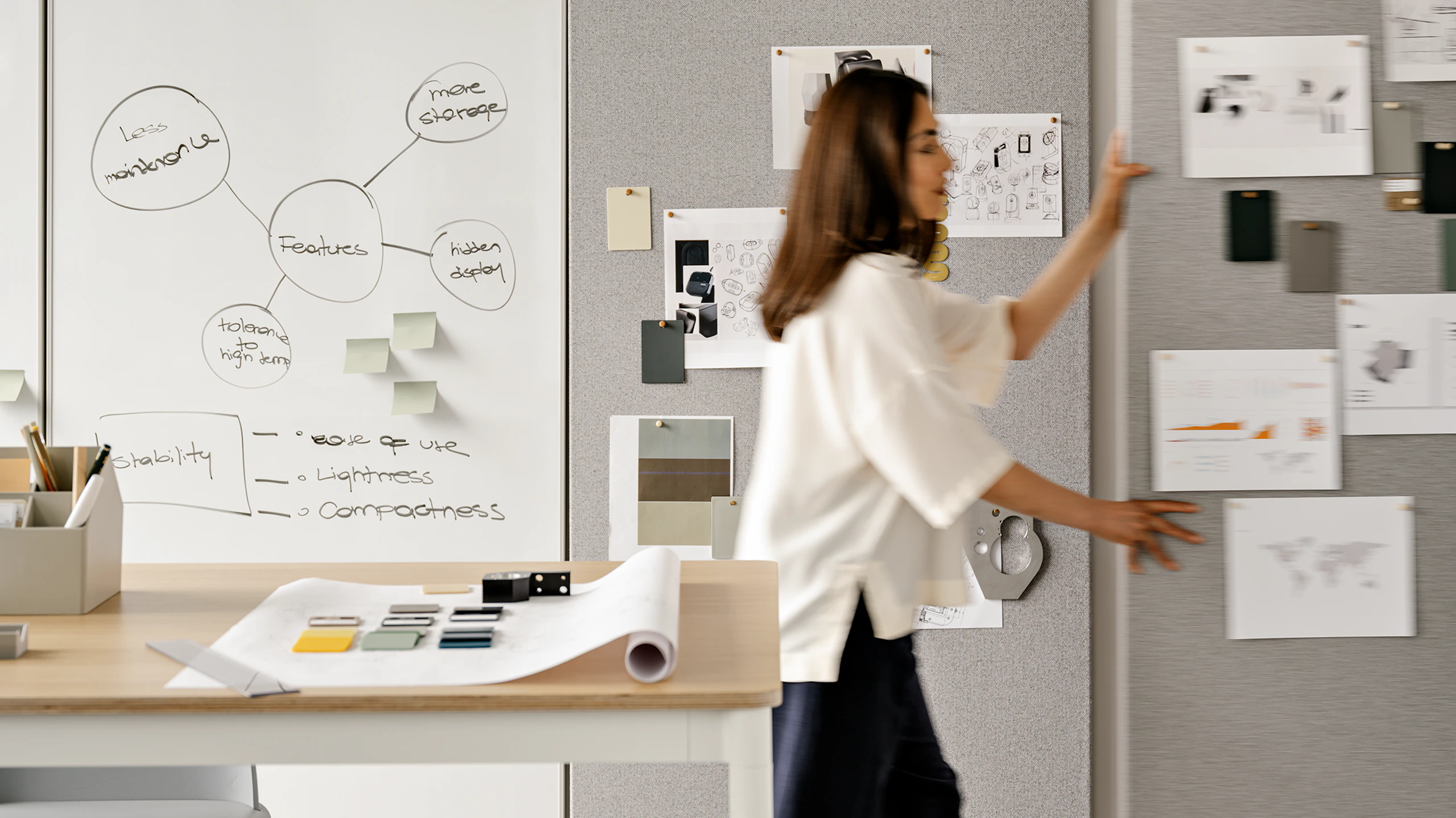 A woman pushing a grey OE1 wall on casters through an office setting.