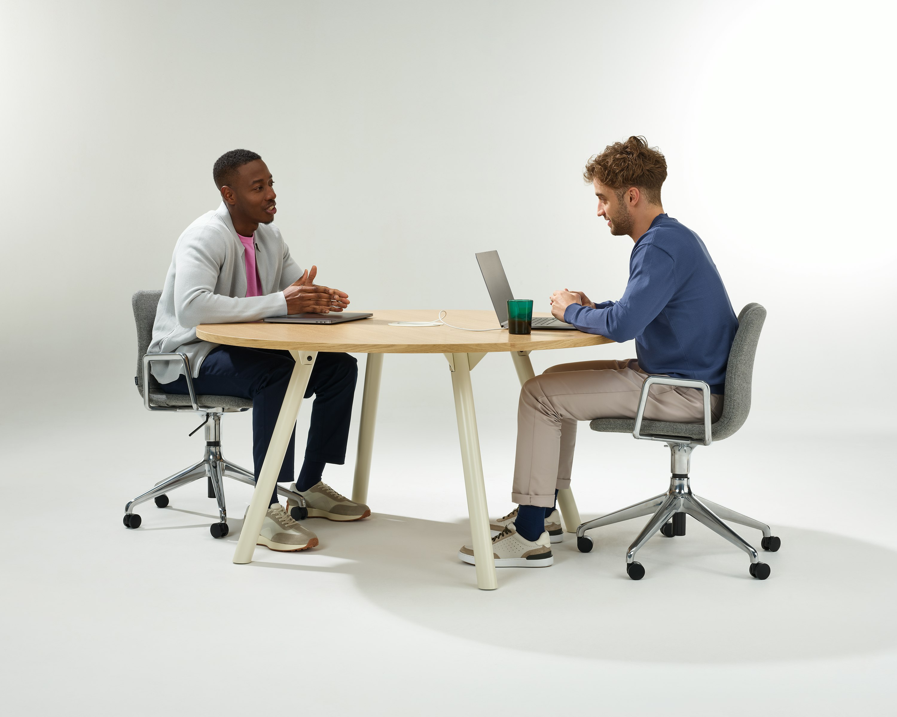 Two people having a meeting around a circular Morse table with oyster legs and an oak veneer top.
