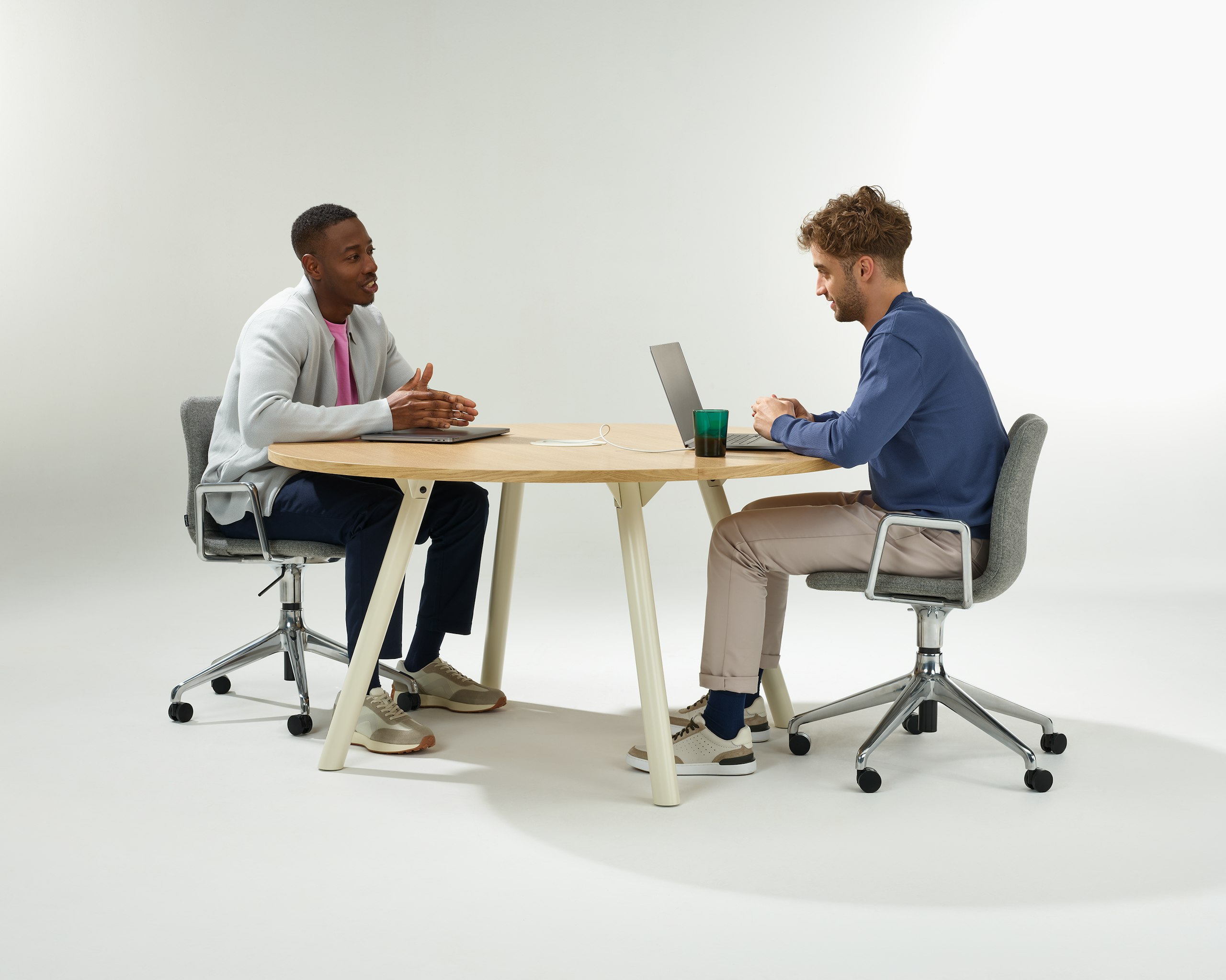 Two people having a meeting around a circular Morse table with oyster legs and an oak veneer top.