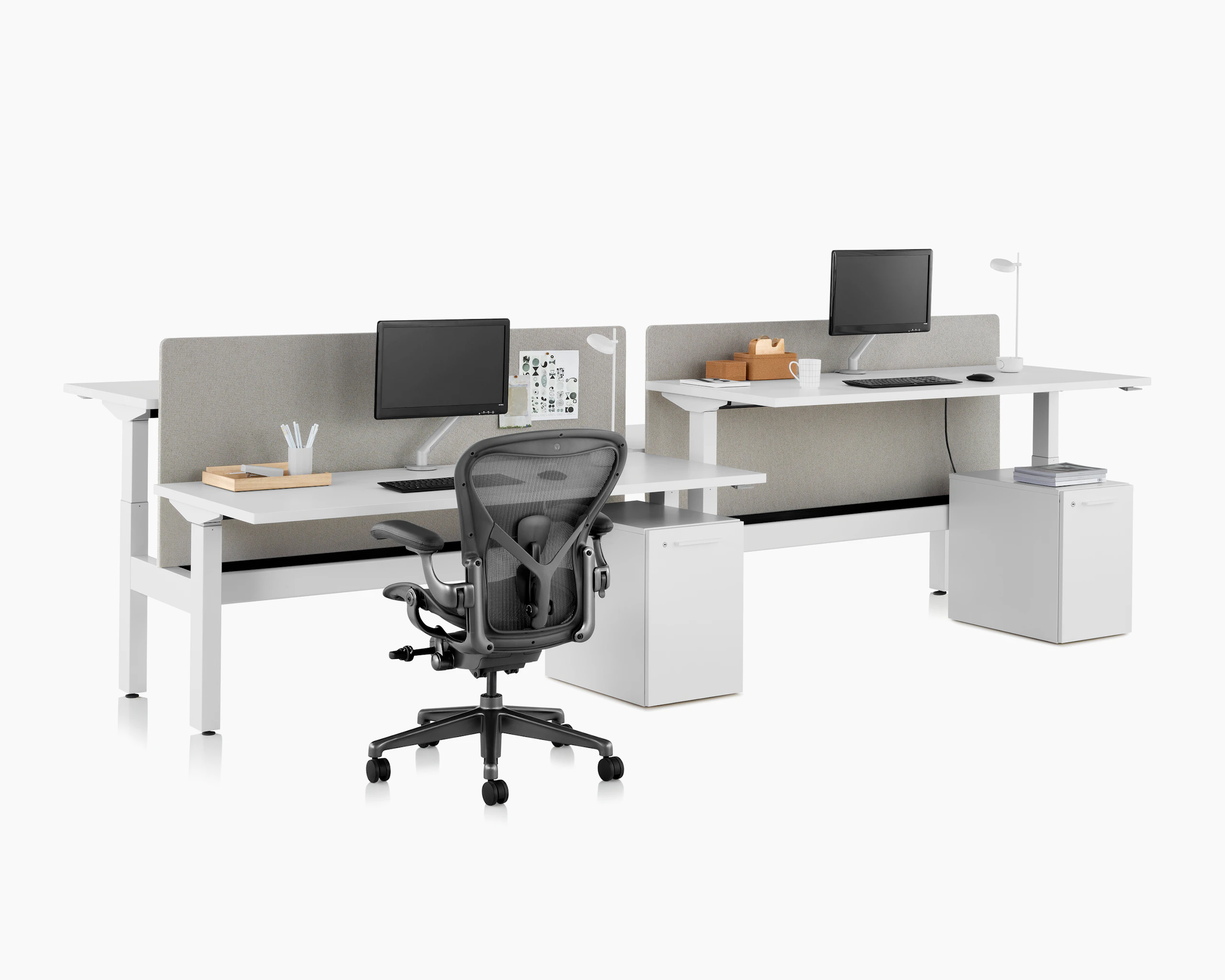 Standing desk system, Nevi Link, with privacy screens, monitors and rectangular work surfaces. Two of the four desks are raised at a standing height.