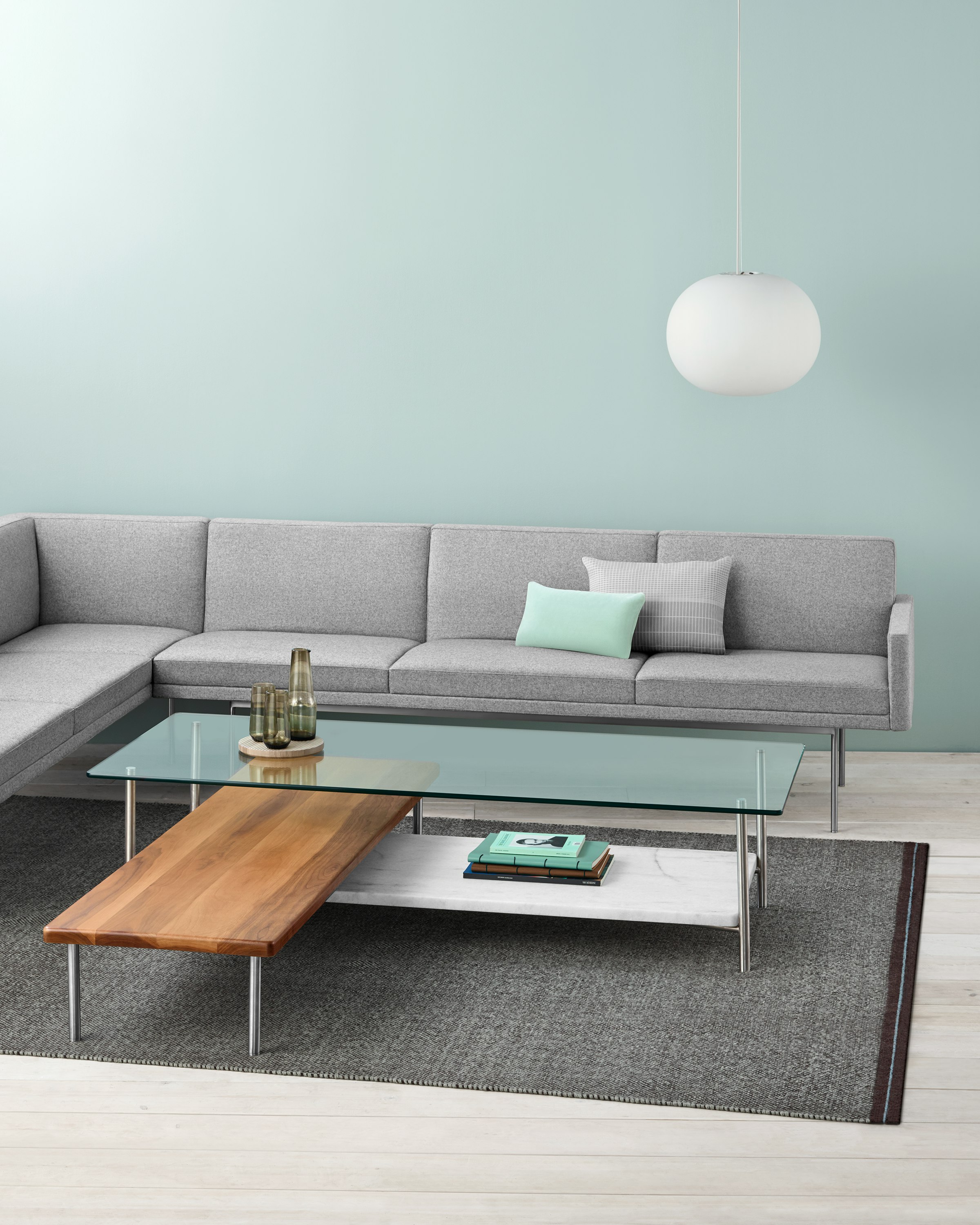 A light gray sectional borders an L-shaped Layer coffee table with three intersecting shelves of glass, wood, and marble.