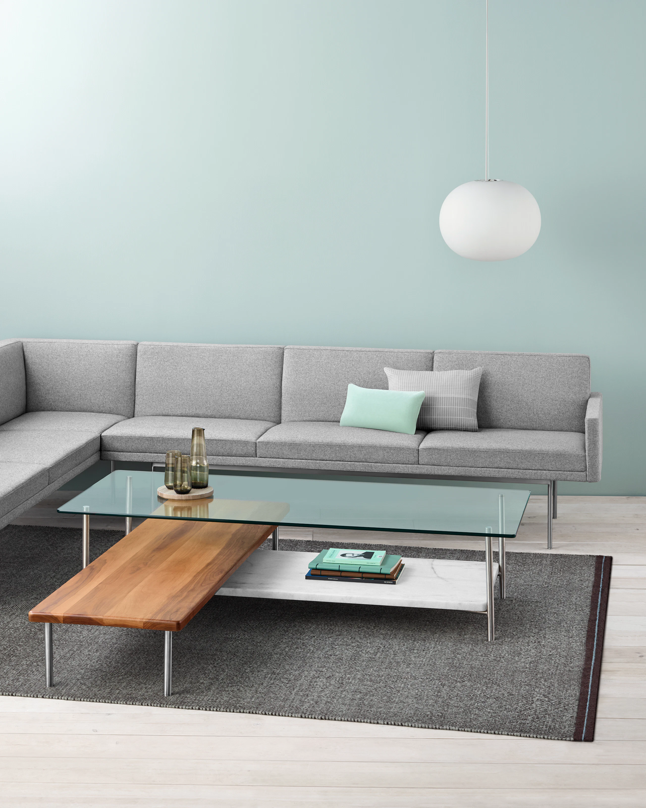 A light gray sectional borders an L-shaped Layer coffee table with three intersecting shelves of glass, wood, and marble.