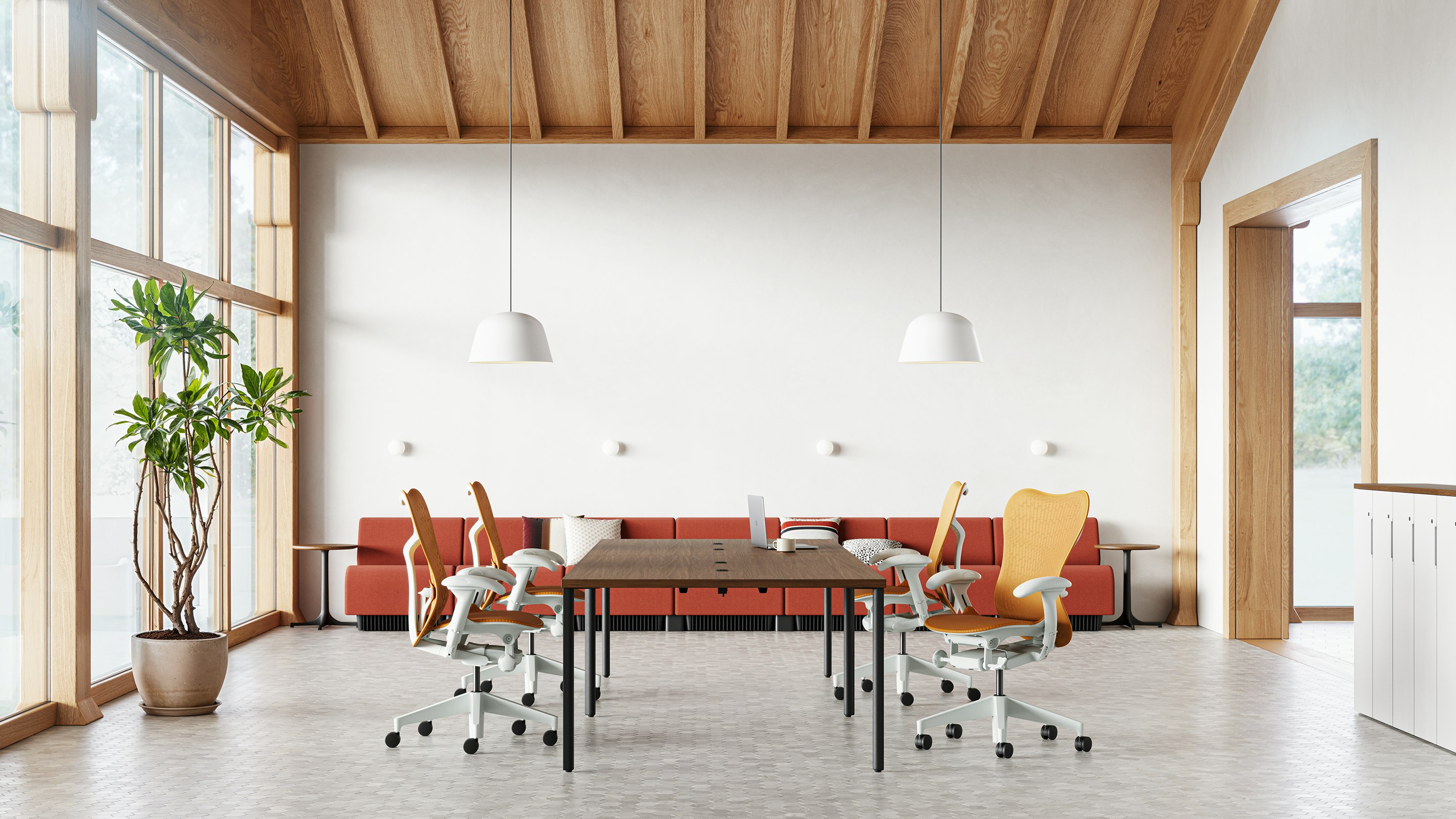 Four Mirra 2 chairs in ochre surround an OE1 table in the middle of a collaborative space with a Chadwick sofa in the back .