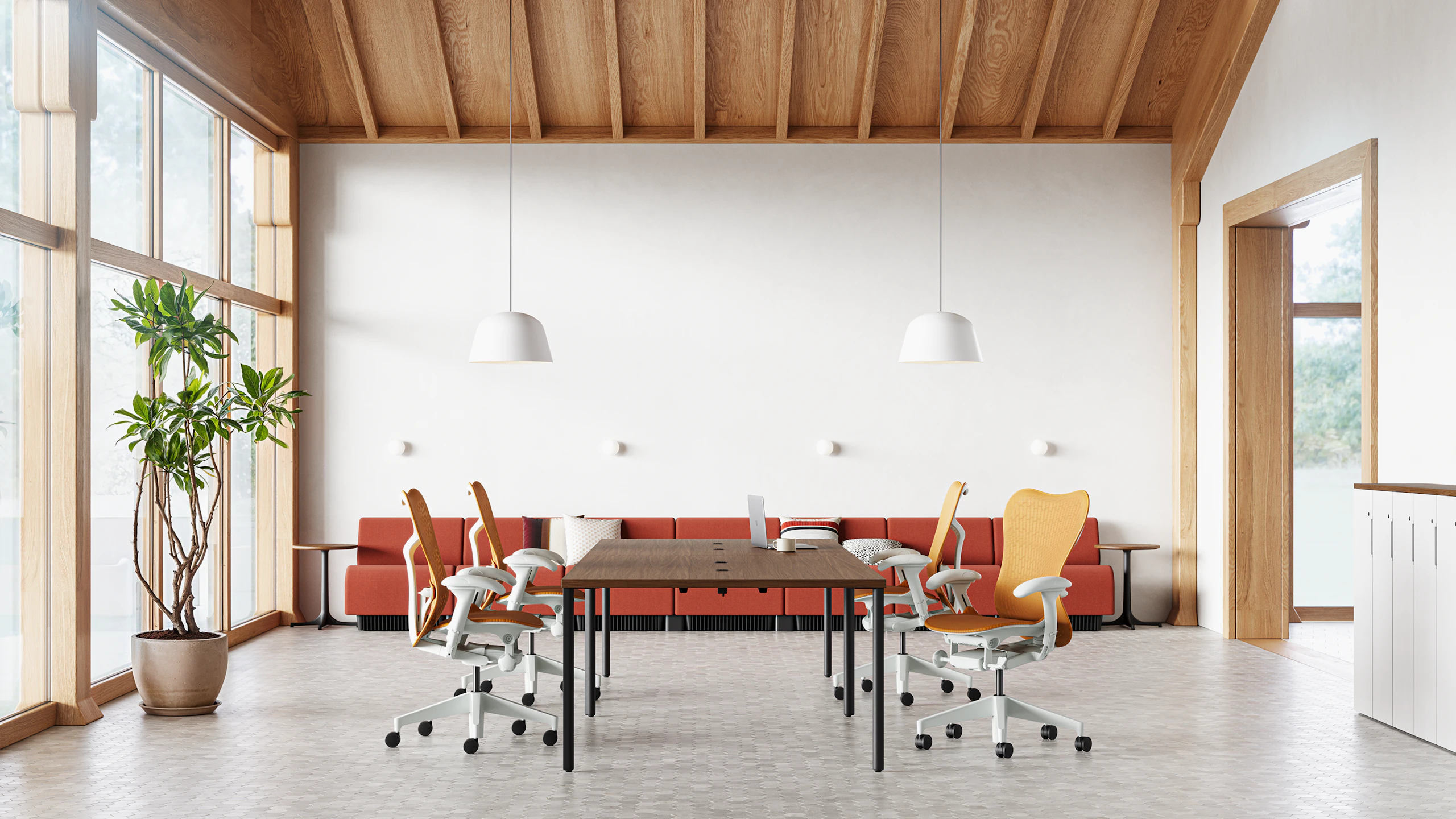 Four Mirra 2 chairs in ochre surround an OE1 table in the middle of a collaborative space with a Chadwick sofa in the back .