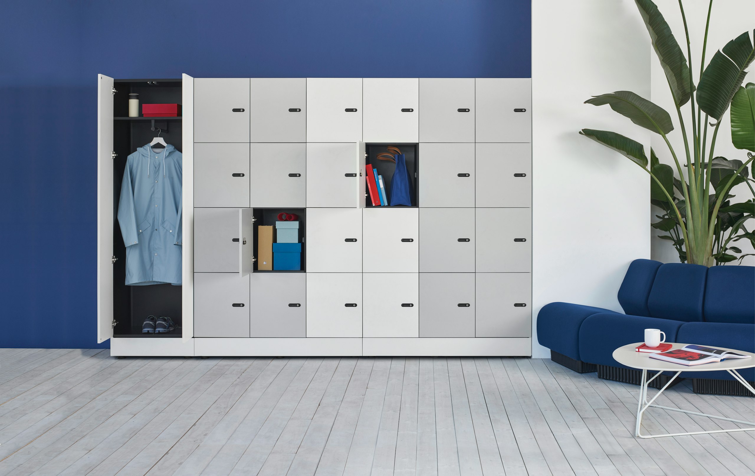 A wall of Port Storage System units consisting of w6 x h4 lockers olus hinge door unit which against a blue wall and next to the lounge sofa area.