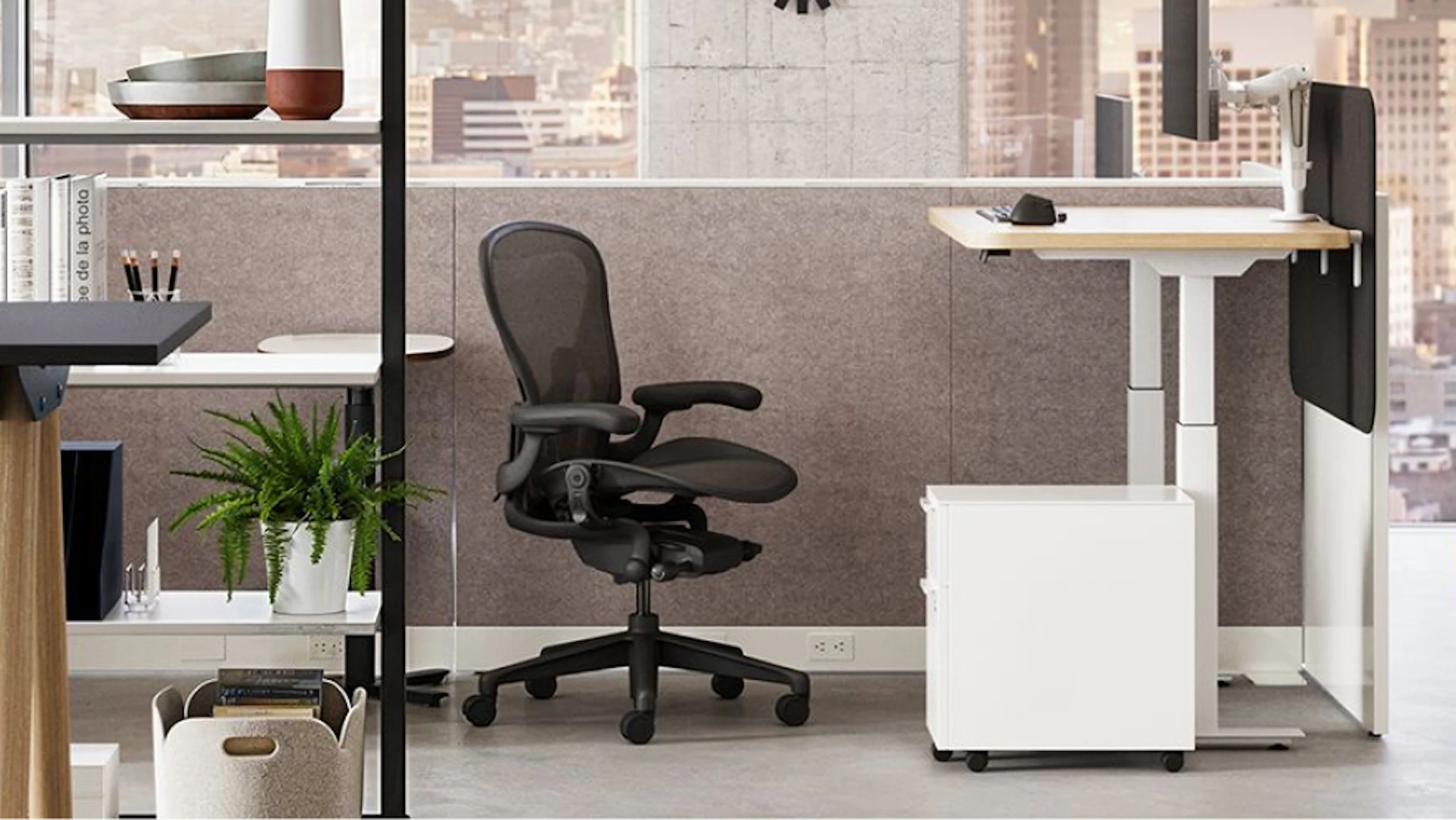 A brightly lit neighbourhood workspace – designed to emphasise employee wellbeing – featuring a sit-to-stand table and Herman Miller Aeron chair overlooking a cityscape