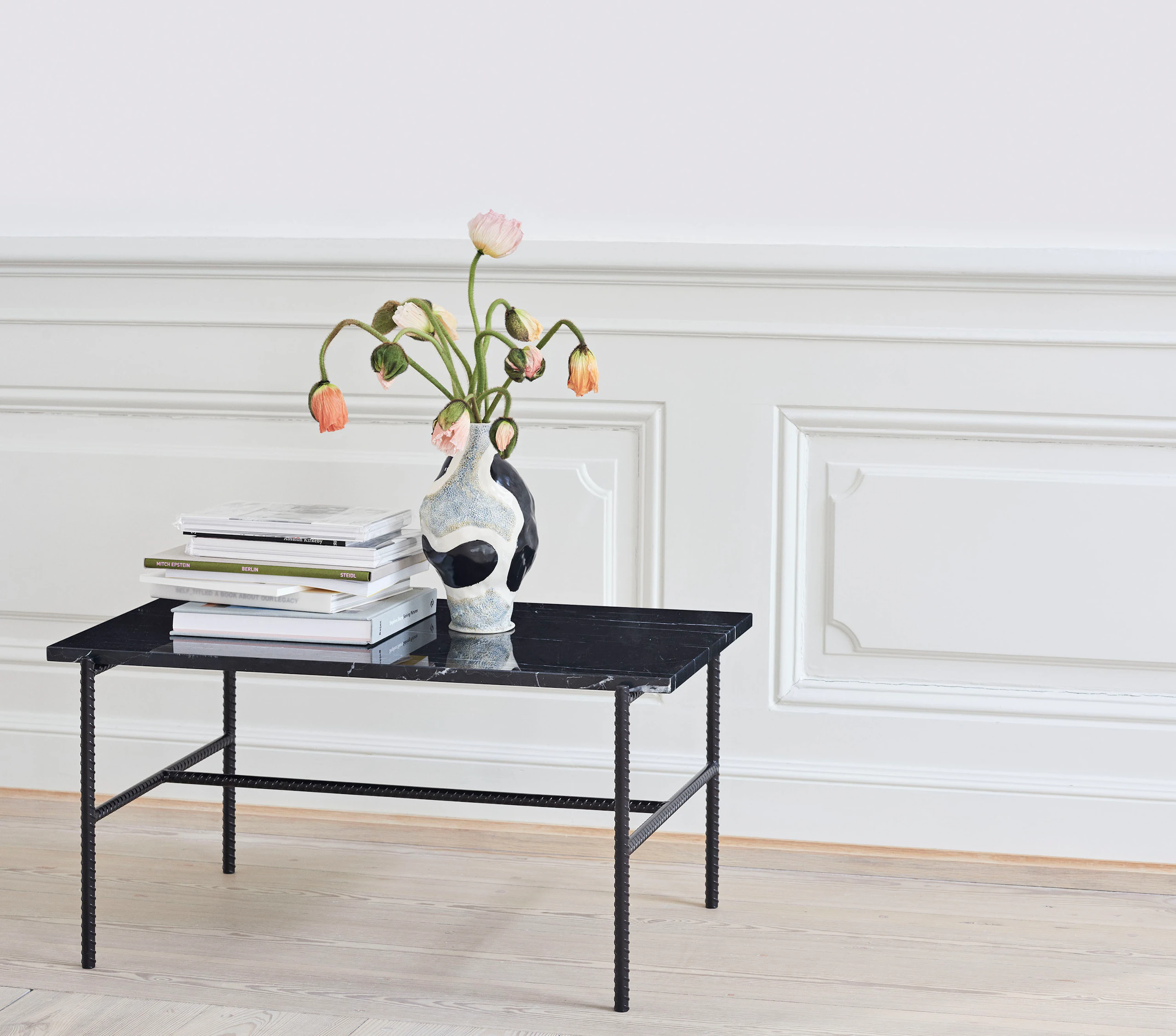 A Rebar Side Table with black marble top and black frame that has books and a vase sitting on top.