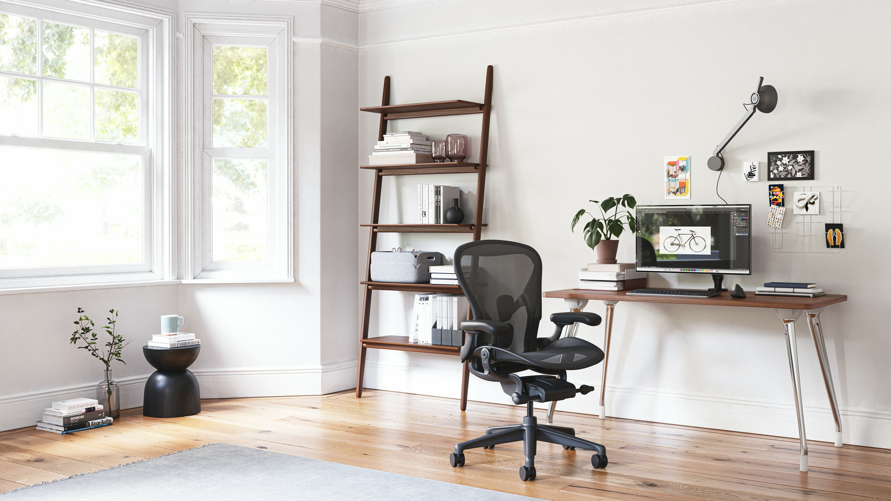 An AbakEnvironments Desk with a walnut top and polised legs, with a graphite Aeron Chair in a light home office setting and Folk Ladder Shelving.