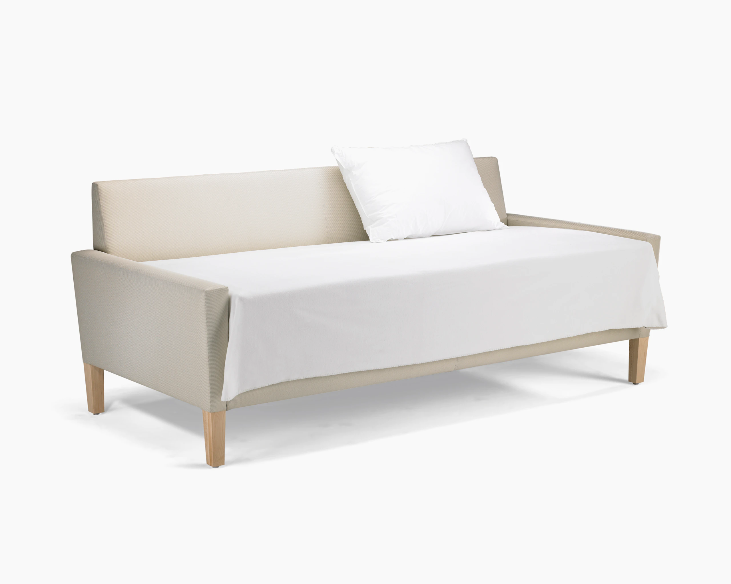 A Brava Flop Sofa in white textile with maple legs converted to sleep surface with sheets and pillow.