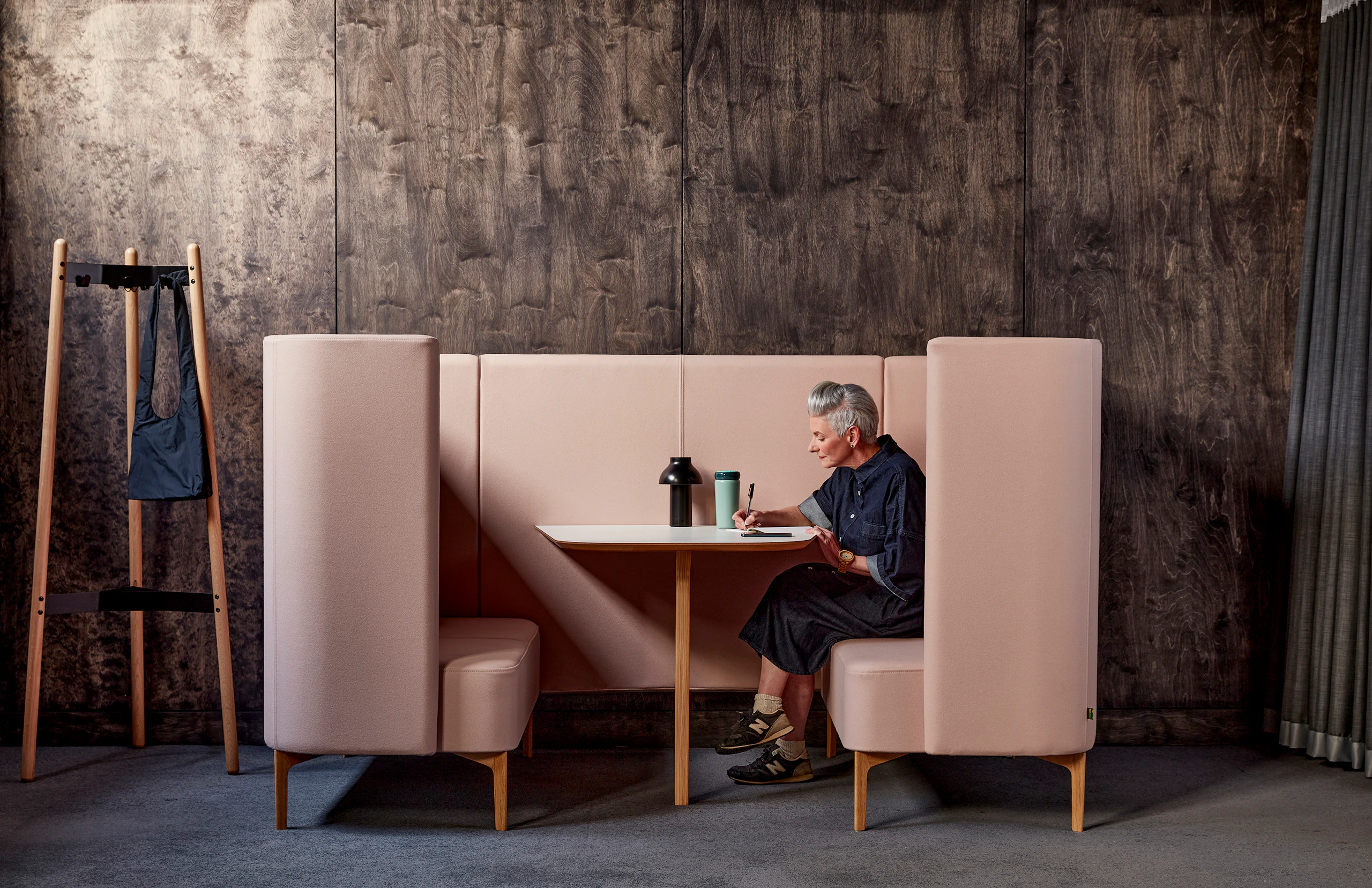 Lady sitting within pale pink Pullman booth with white table top and oak legs.