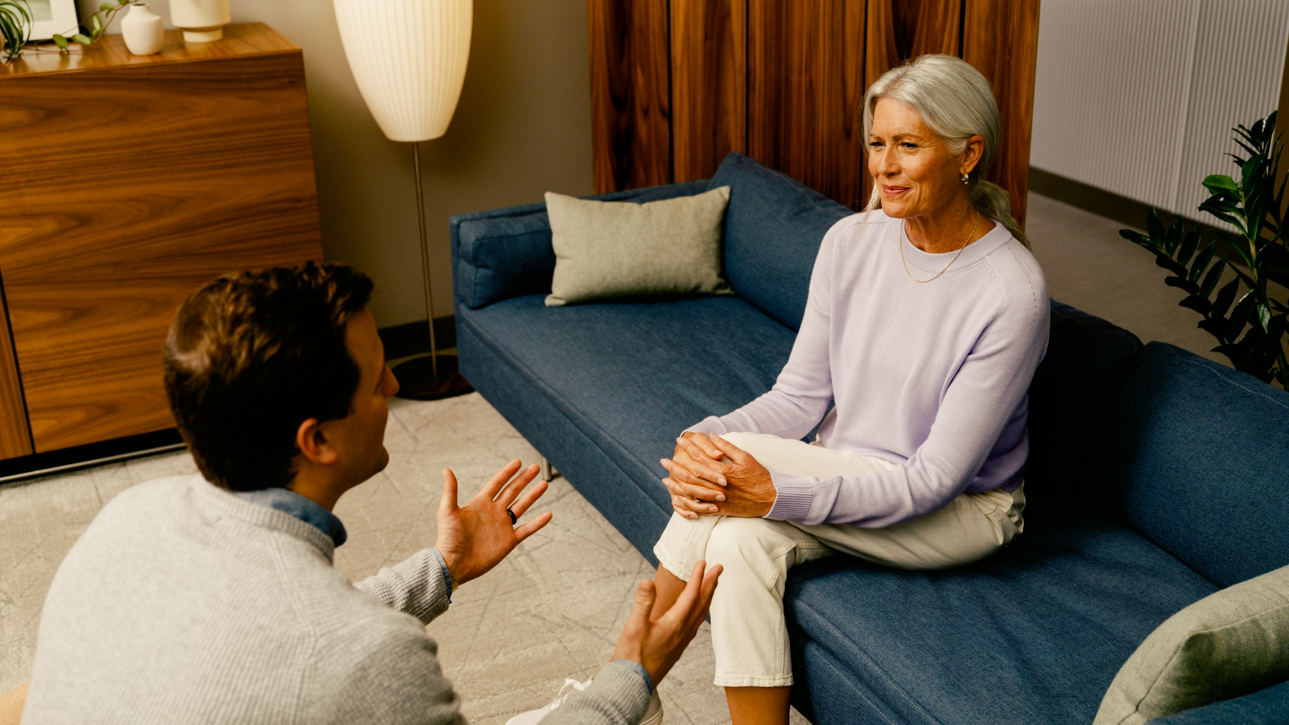 Male receptionist greeting a female patient in a healthcare waiting area.